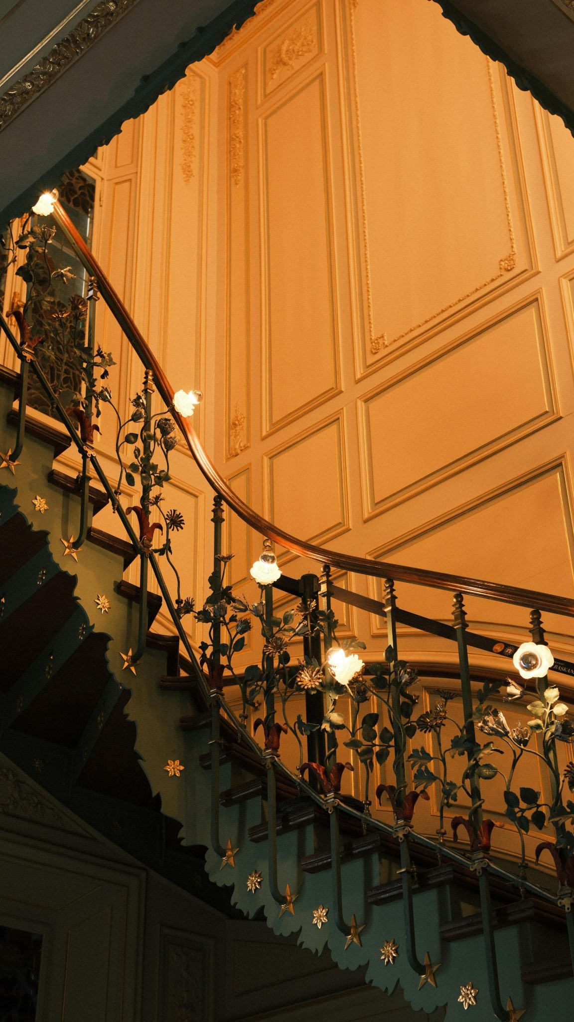 A beautifully illuminated staircase featuring intricate floral metal railings indoors.