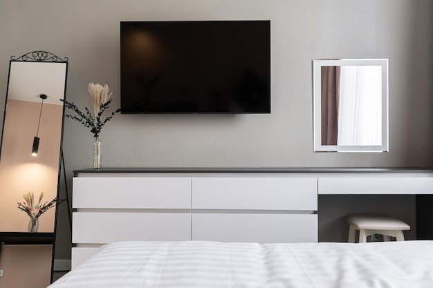 A bedroom with a white dresser and a large television on the wall | Premium Photo