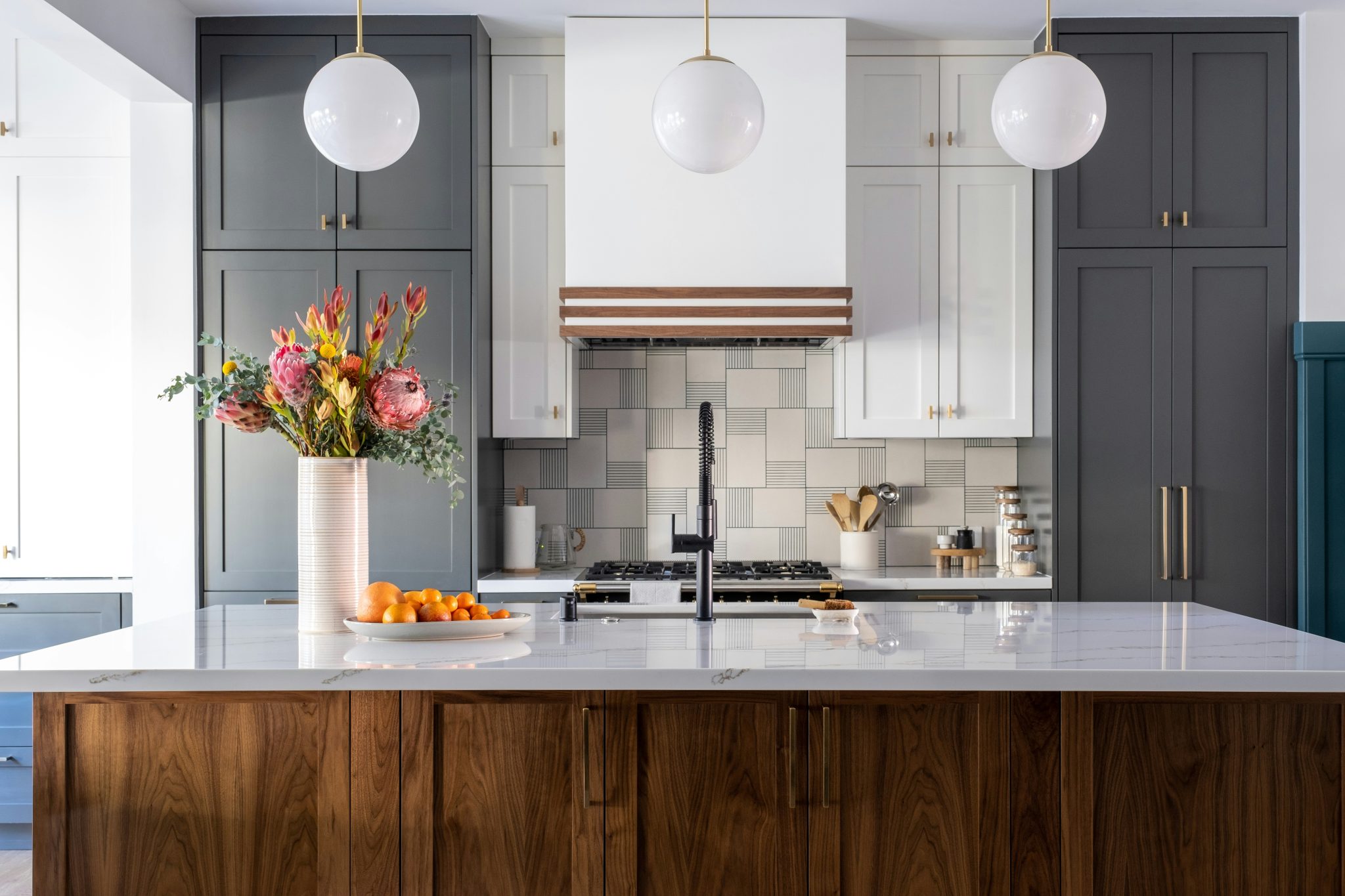 A bright kitchen featuring a pristine white countertop, complemented by a charming flower vase. Three elegant hanging lamps illuminate the space, casting a warm glow.