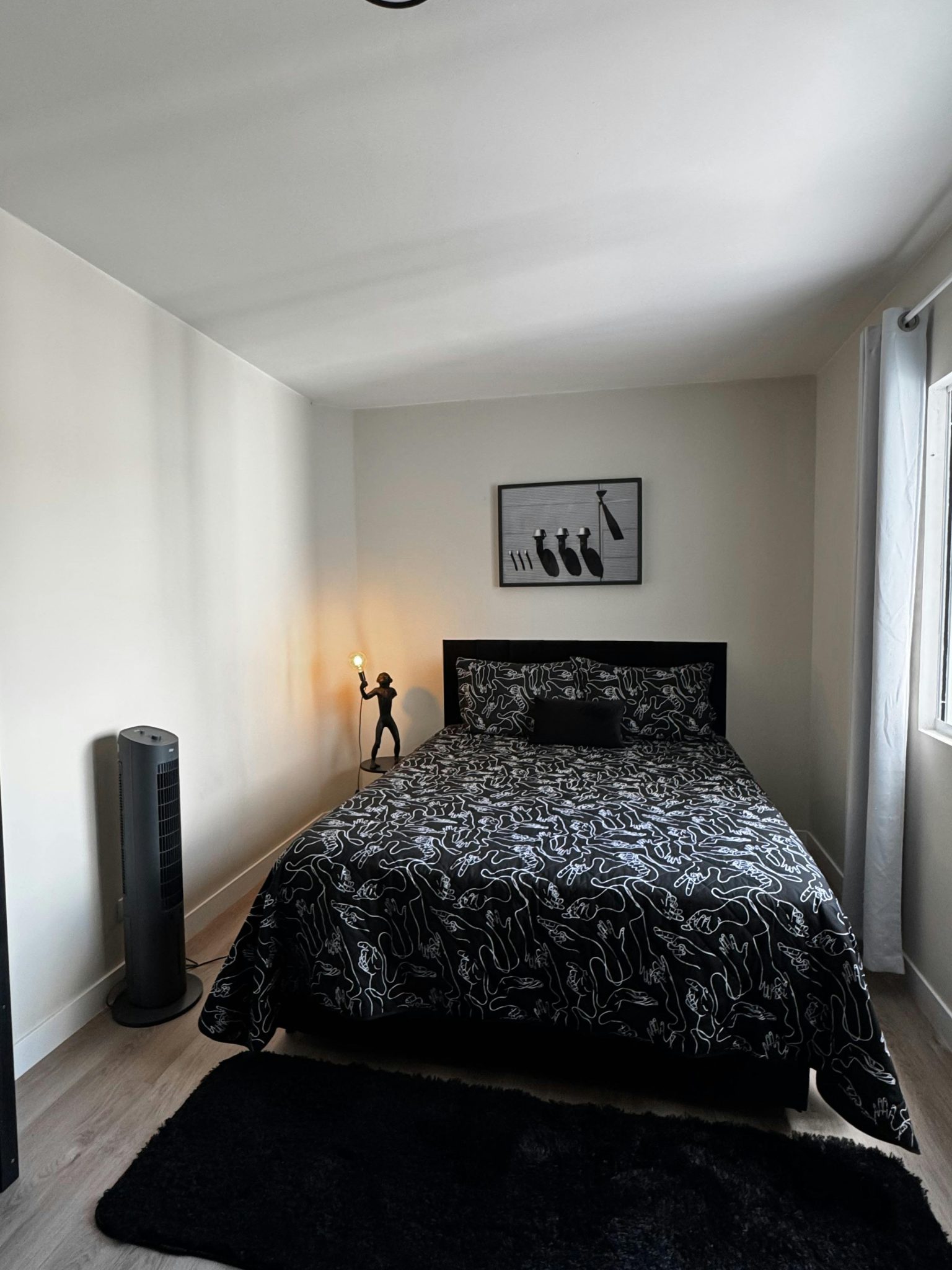 A bright, minimalist bedroom featuring abstract-patterned bedding, a stylish lamp, and modern decor.