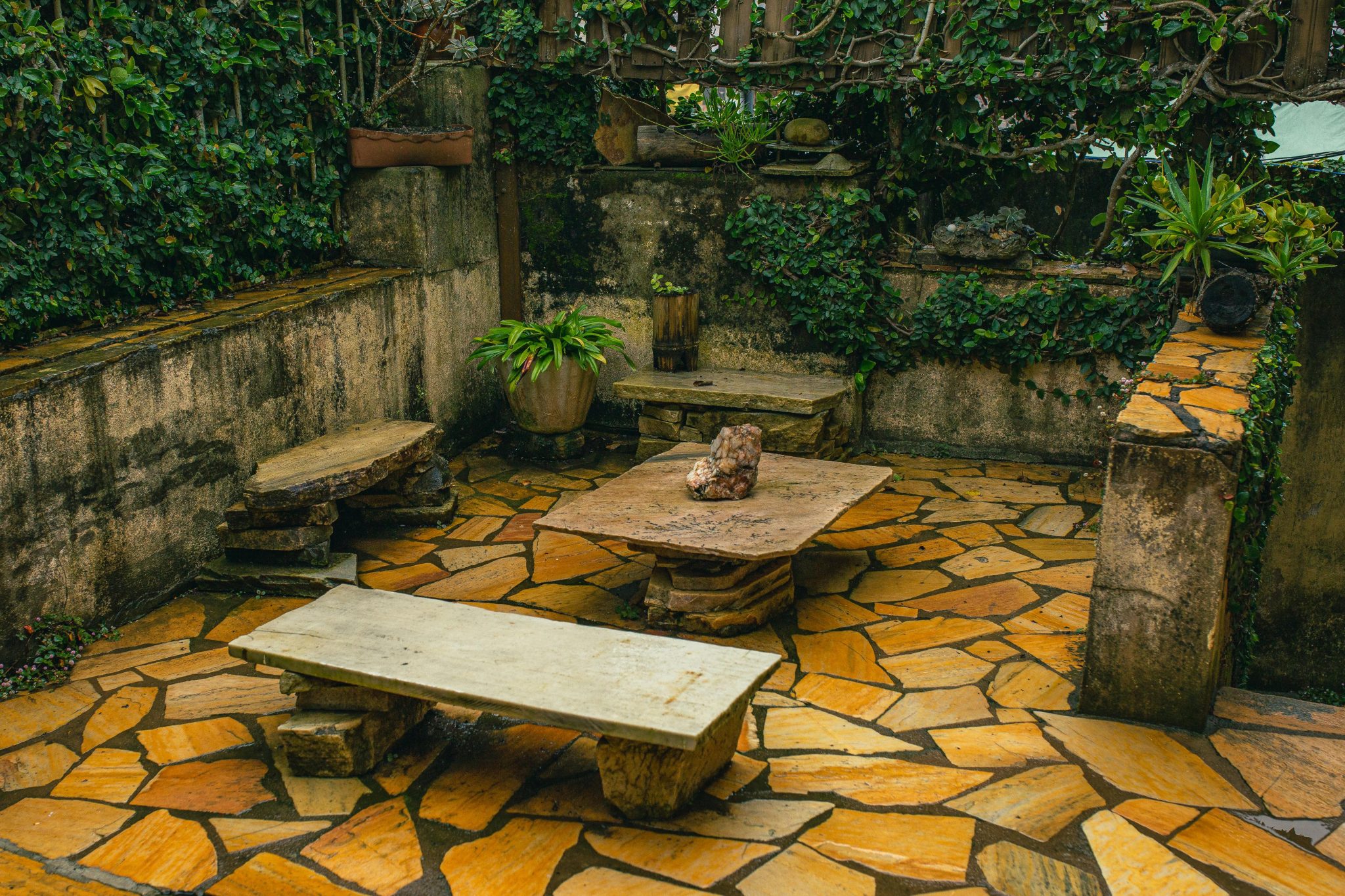 A cozy stone garden patio with ivy-covered walls, stone benches, and rustic decor perfect for relaxation.
