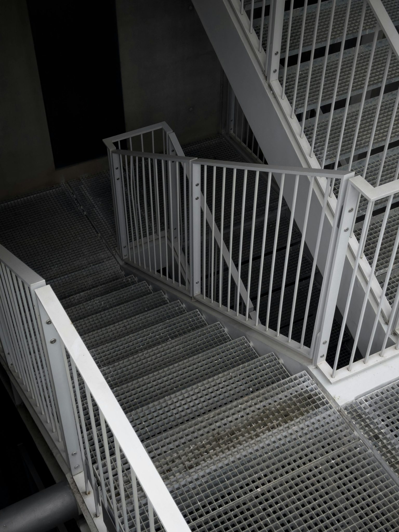 A detailed view of an industrial metal staircase with white handrails and mesh steps indoors.