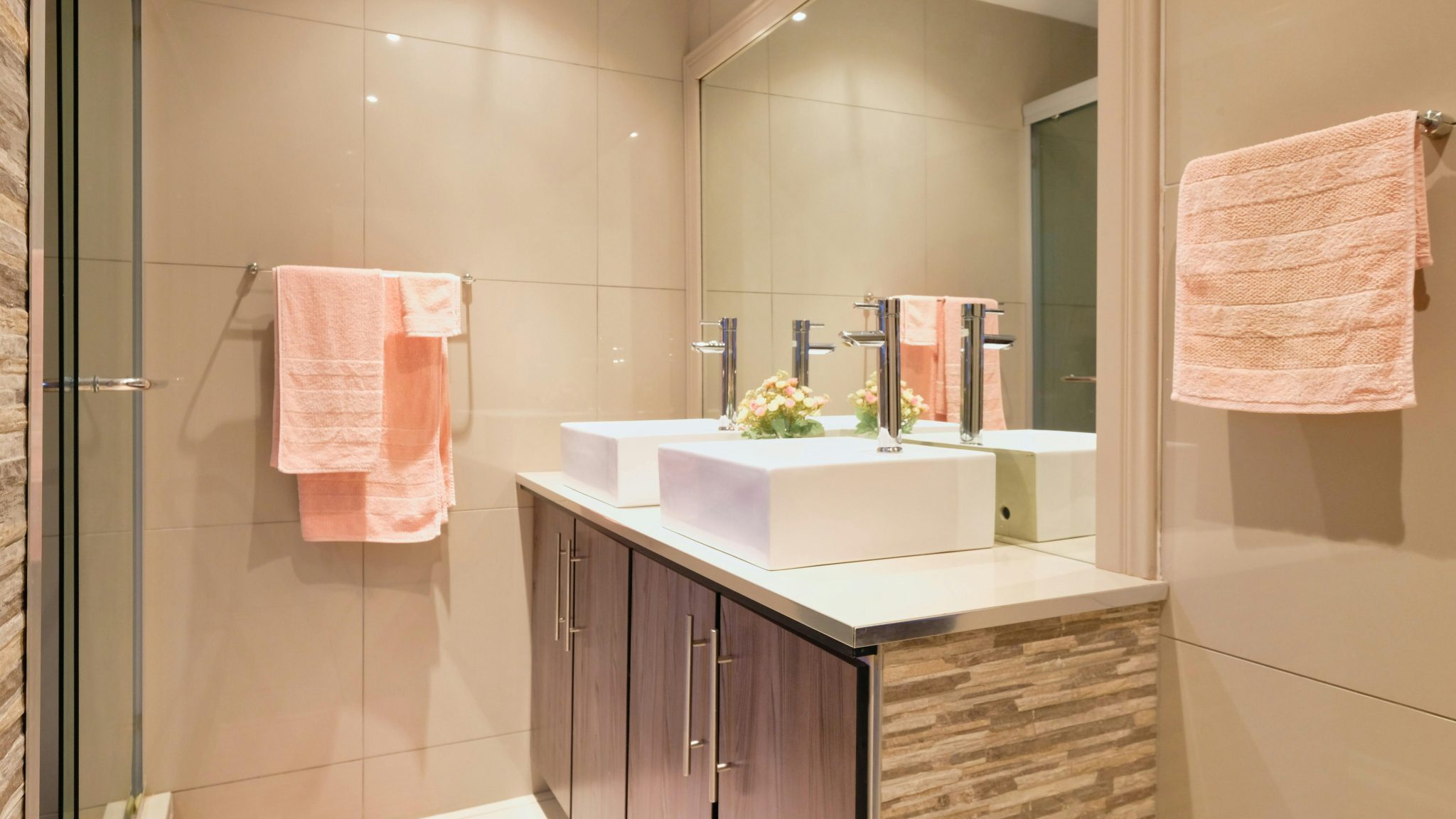A modern bathroom featuring double sinks, large mirror, and peach towels enhancing elegance.