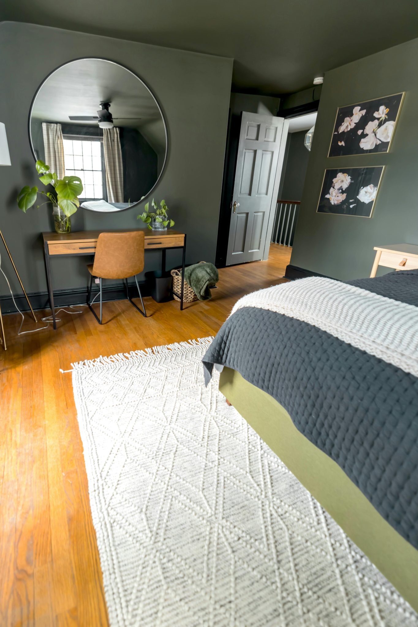 A modern bedroom with stylish decor, featuring a desk, mirror, and potted plants.
