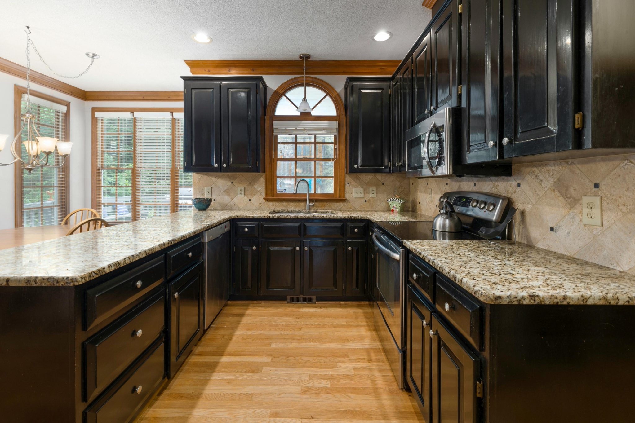 A modern kitchen featuring dark cabinetry, granite countertops, and hardwood floors under bright daylight.