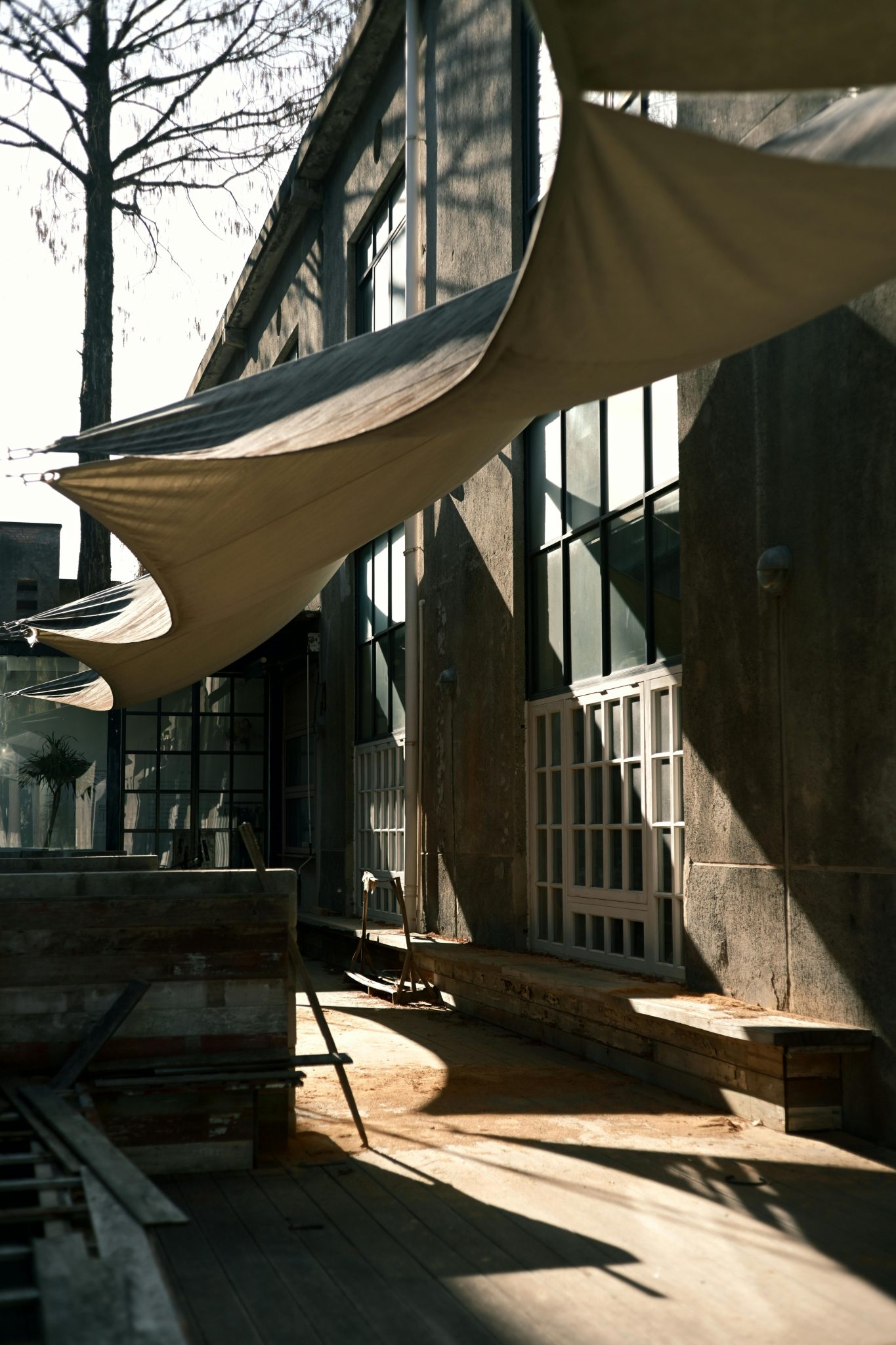 A modern, sunlit outdoor patio with shade canopies and architectural details casting shadows.
