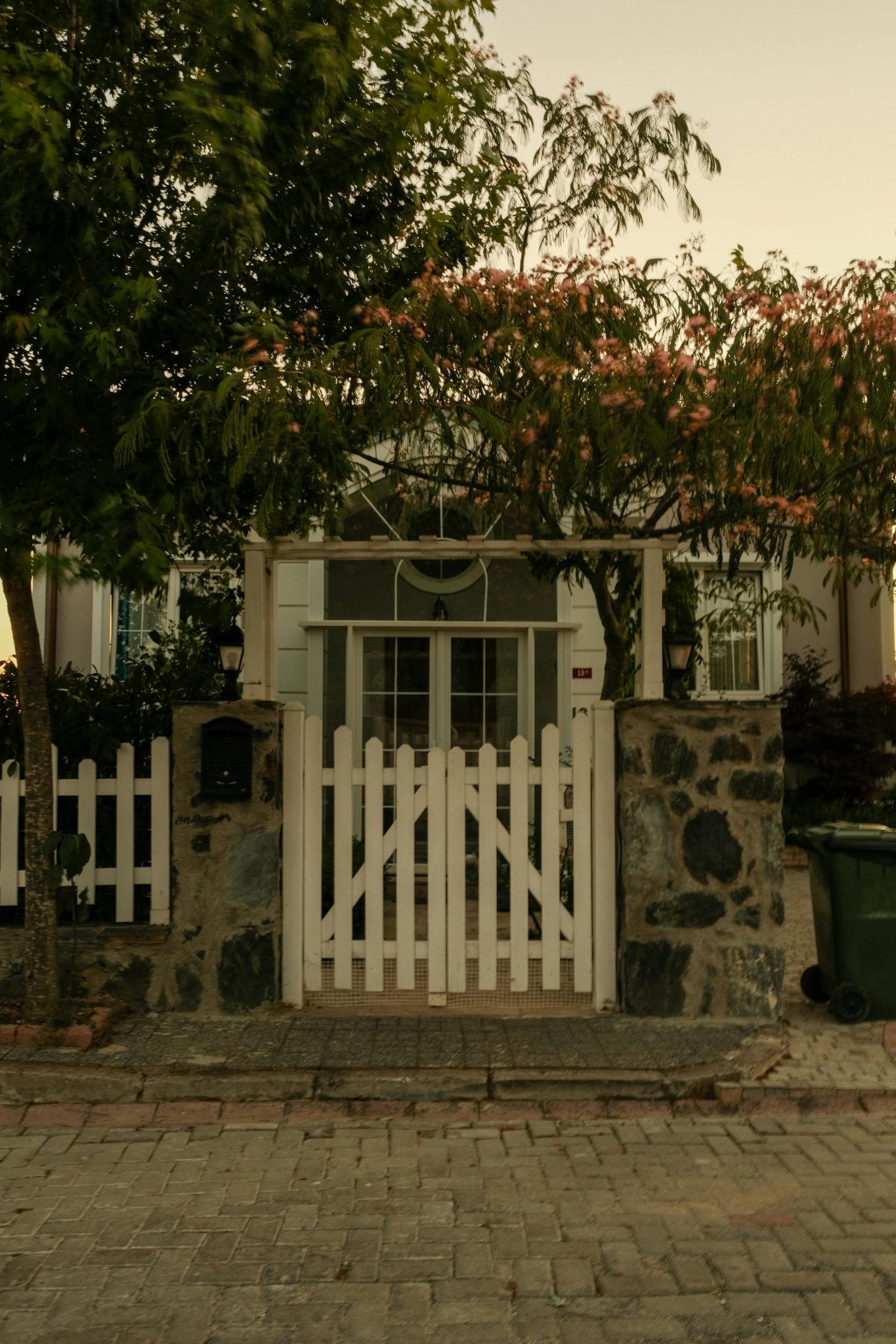 A picturesque entrance with a white picket gate and cobblestone path leading to an urban house.