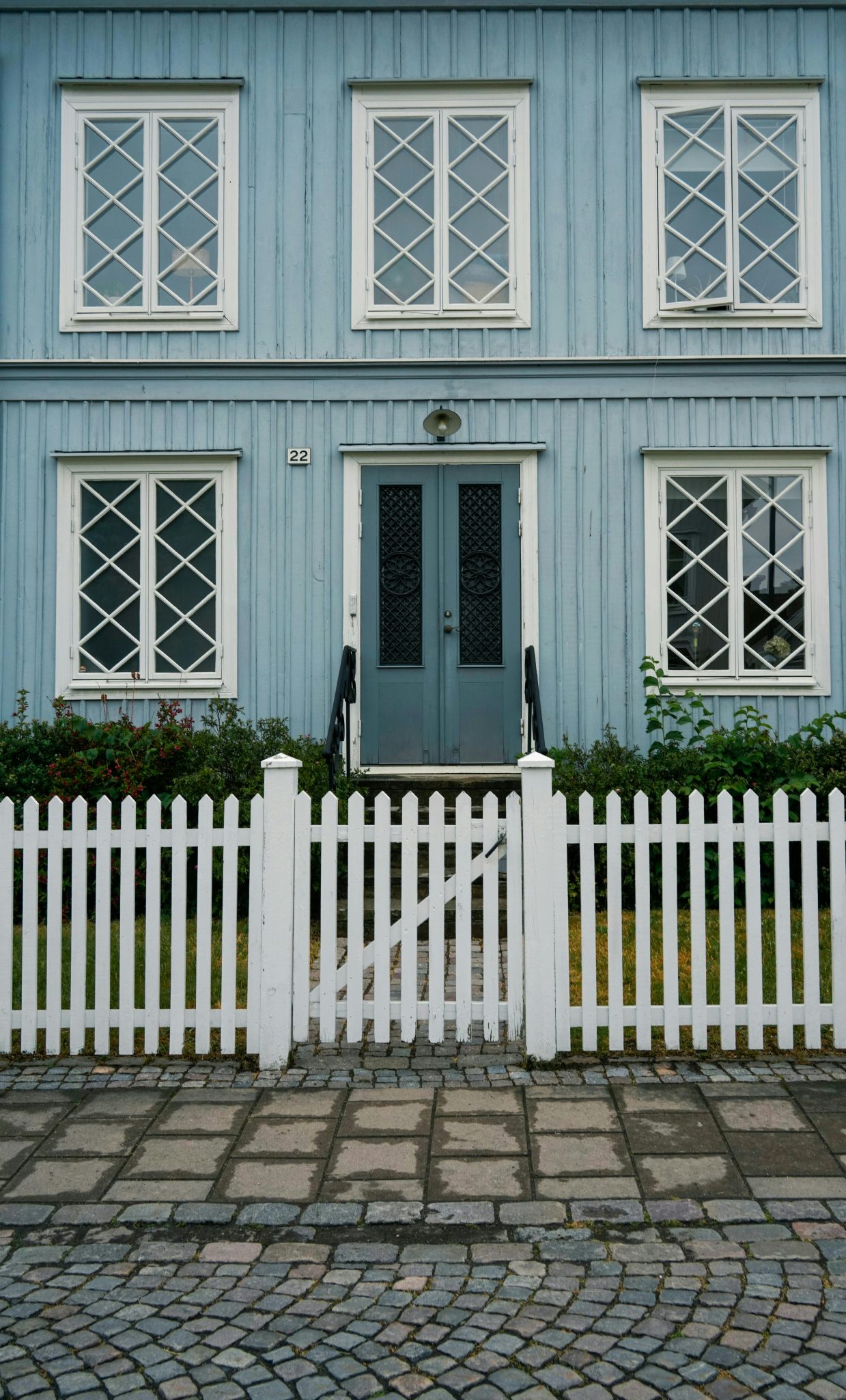 A quaint cyan house facade with a picket fence and large windows, offering a classic estate look.