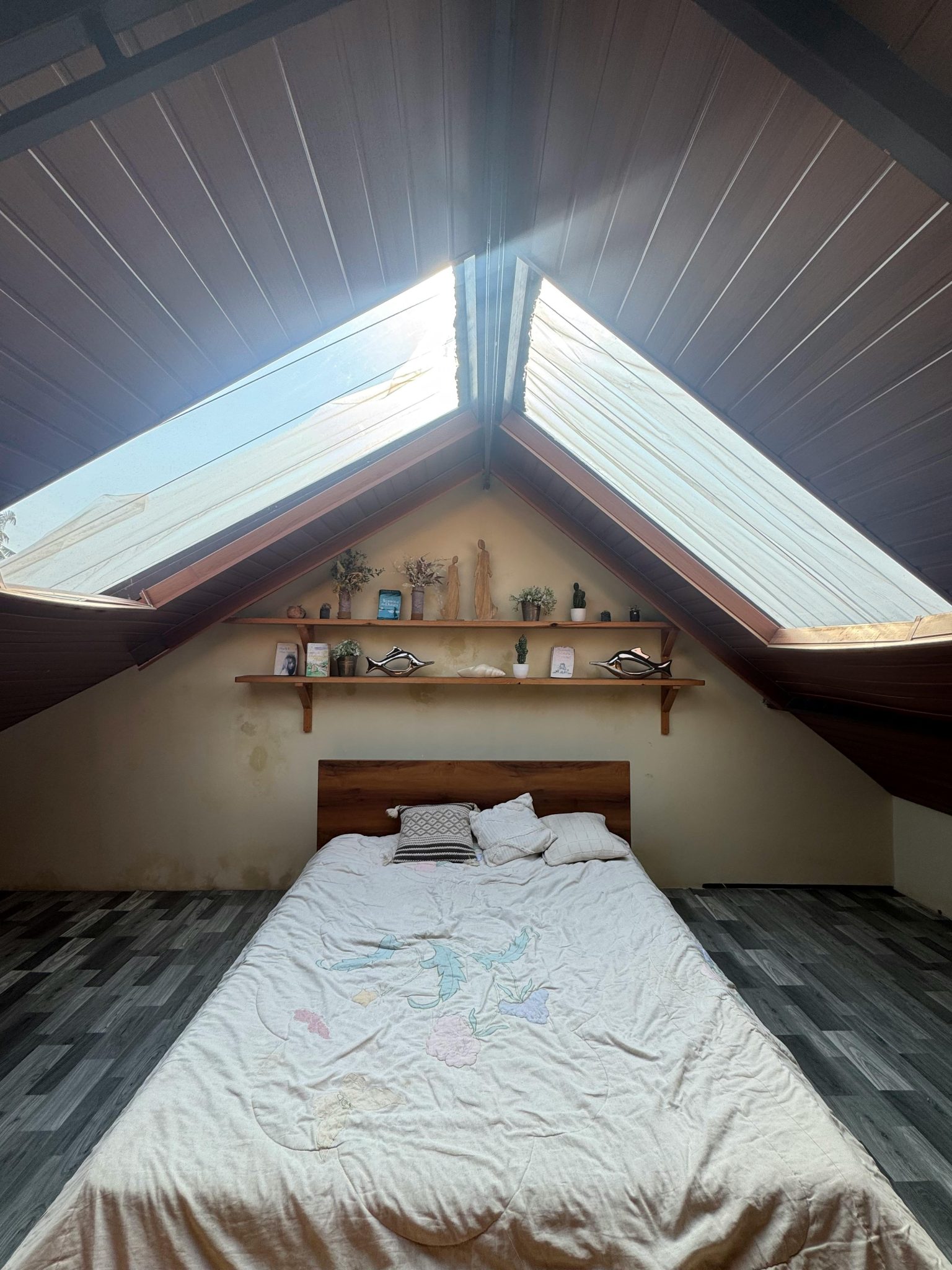 A serene loft bedroom featuring a double bed under large skylight windows, creating a bright and airy atmosphere.