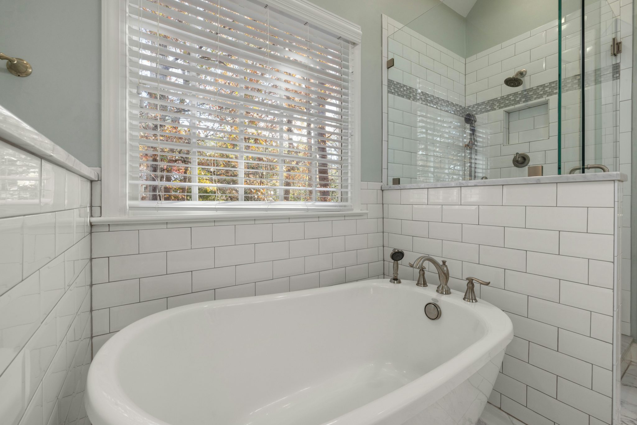 A spacious bathroom featuring a luxurious freestanding tub and glass shower surrounded by subway tiles.
