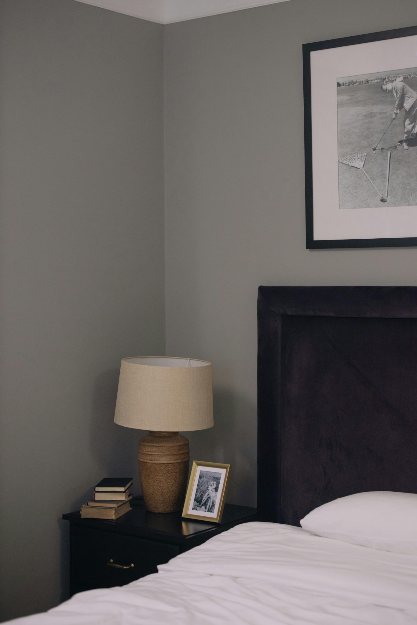 A stylish bedroom featuring a side table with books, lamp, and framed photos.