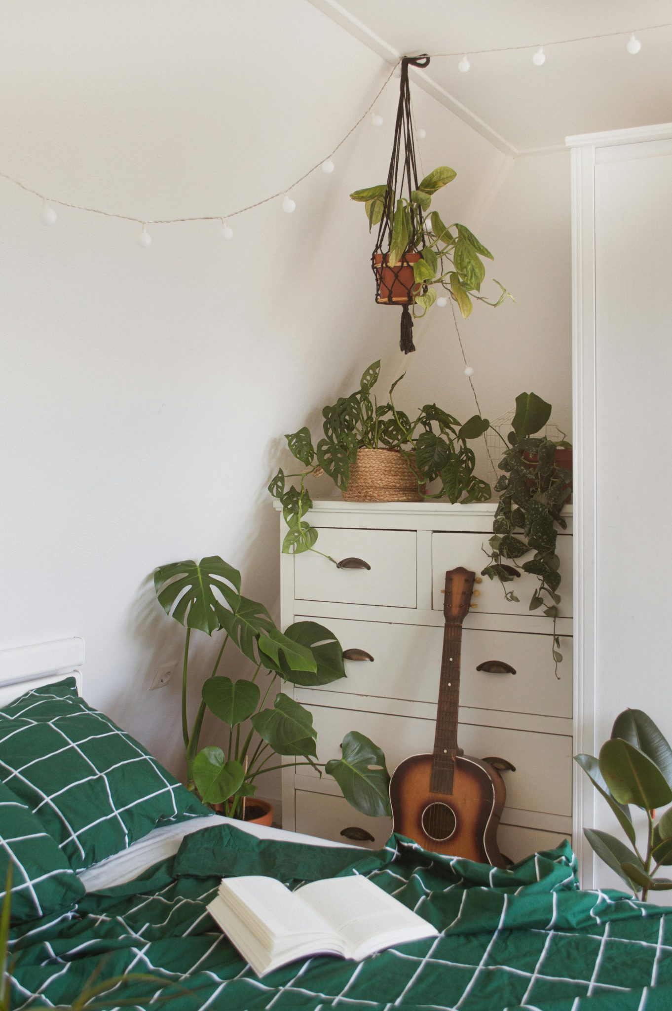 A stylish bedroom featuring houseplants, a guitar, and cozy interior design elements.