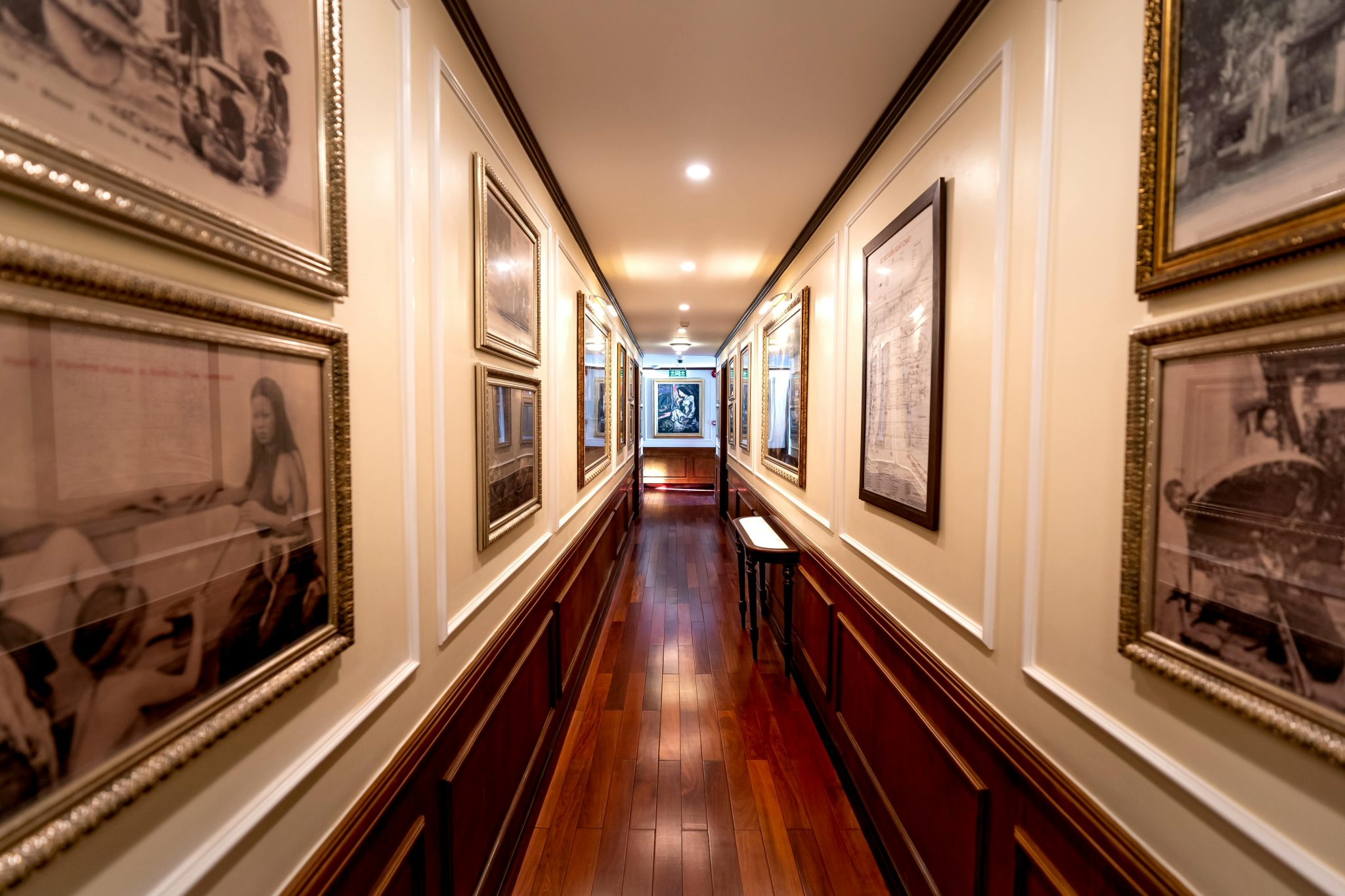 A stylish corridor featuring framed art on illuminated walls and a polished wooden floor.