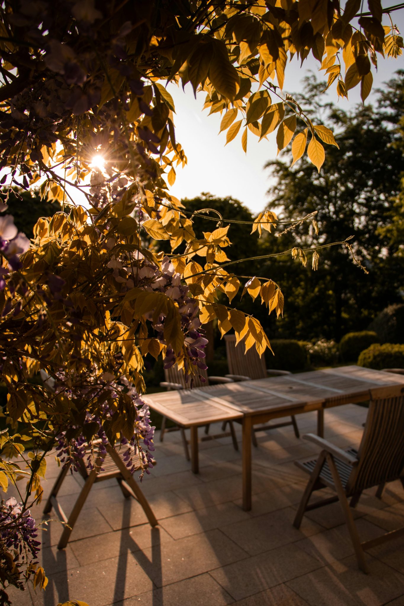 A tranquil patio scene with wooden furniture and golden sunlight filtering through leaves.
