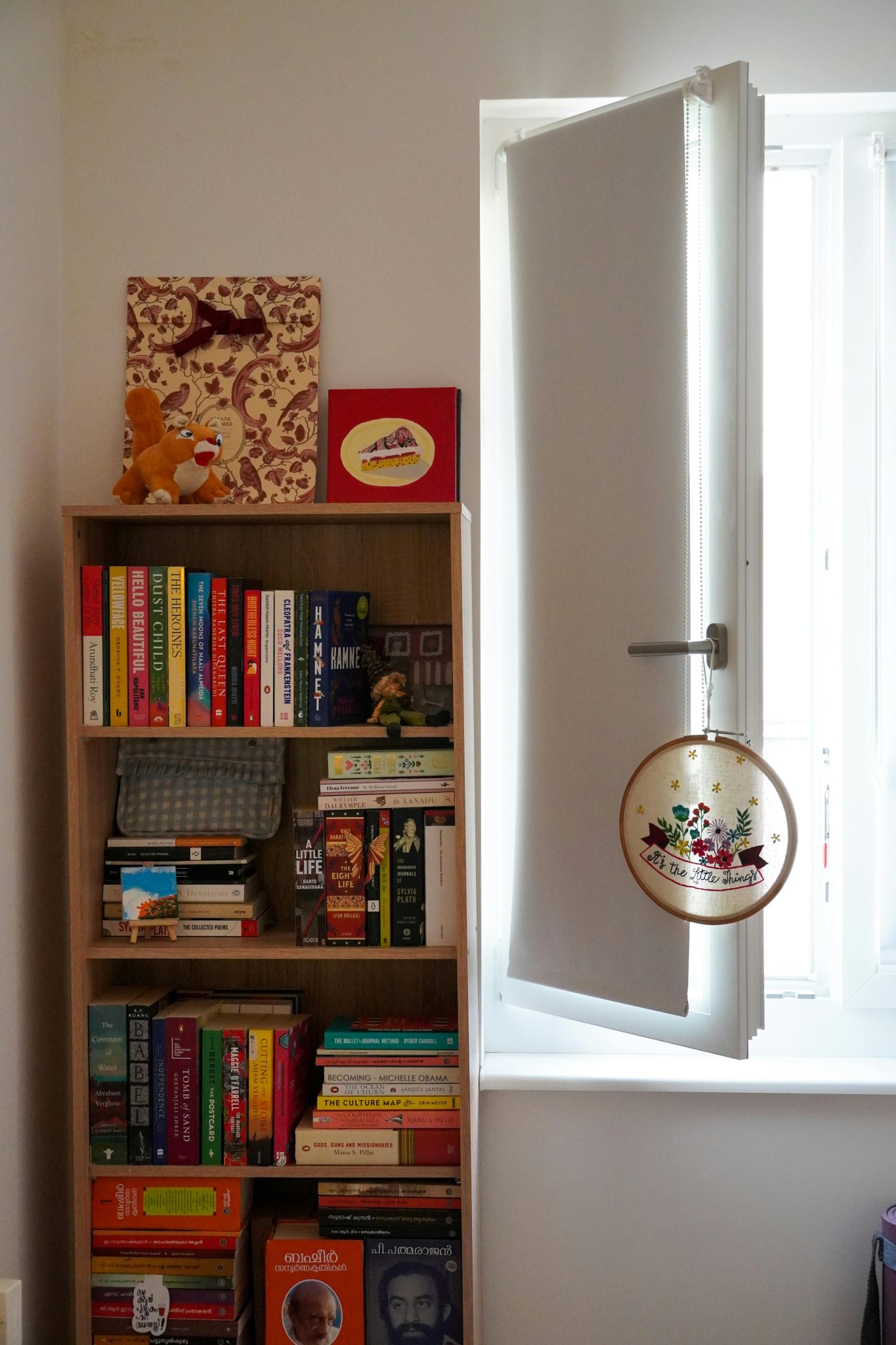 A vibrant bookshelf next to an open window, casting soft daylight indoors.