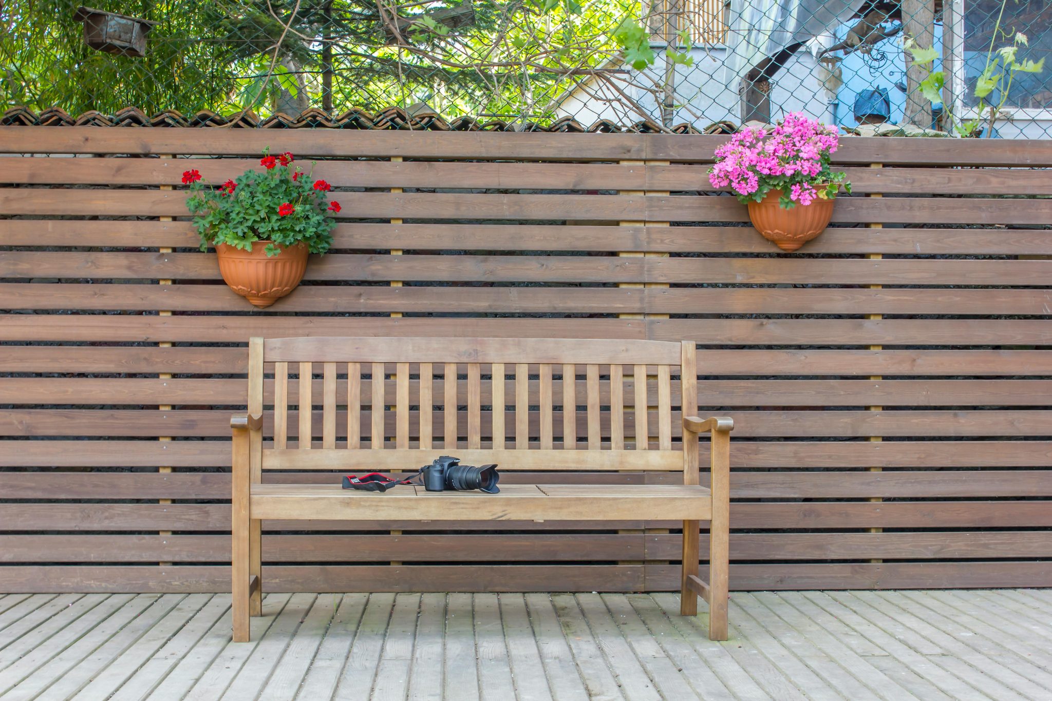 A wooden bench with potted flowers against a wooden fence in a peaceful backyard setting.