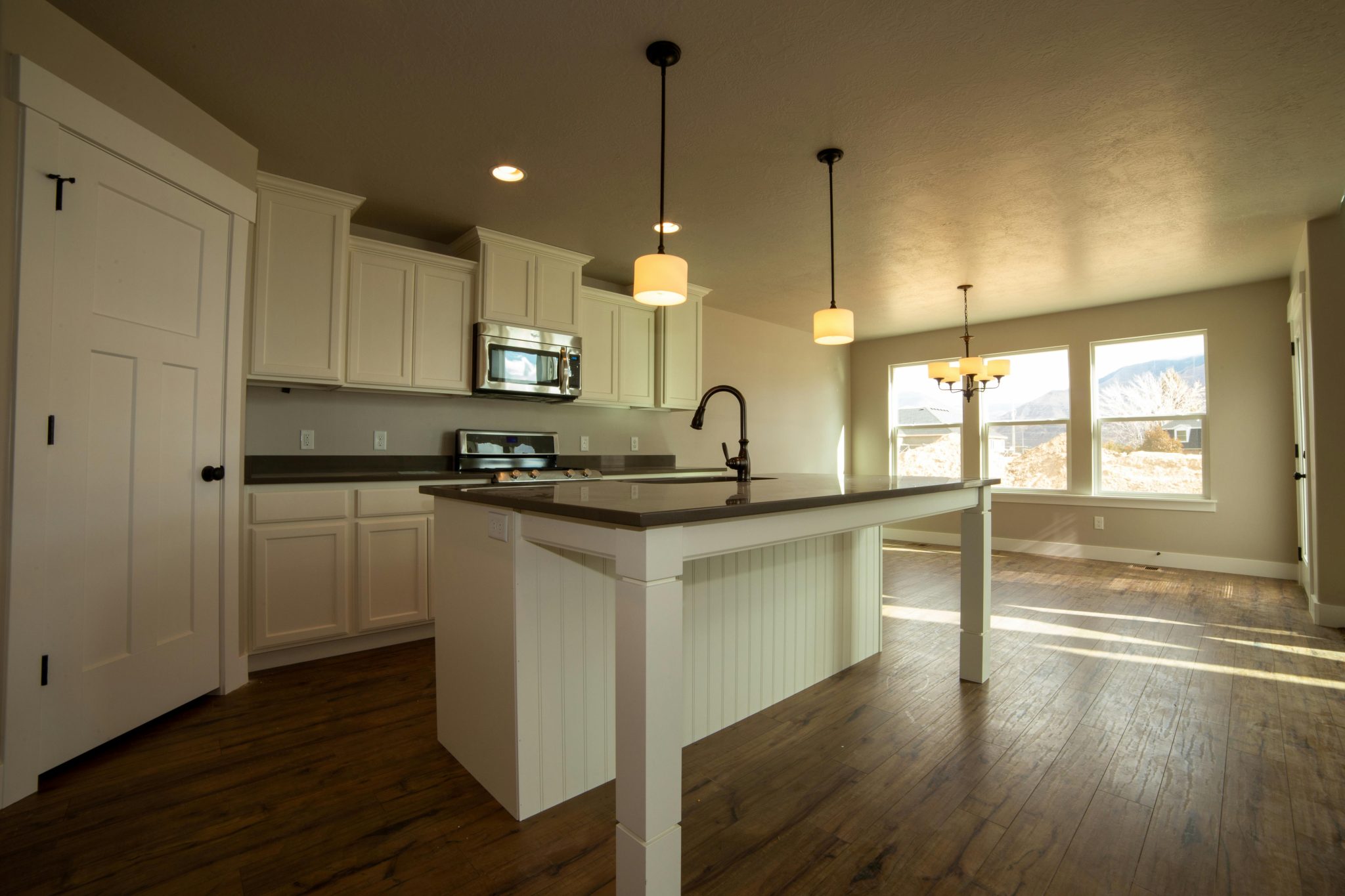 An elegant kitchen with an island, pendant lights, and natural light through large windows.