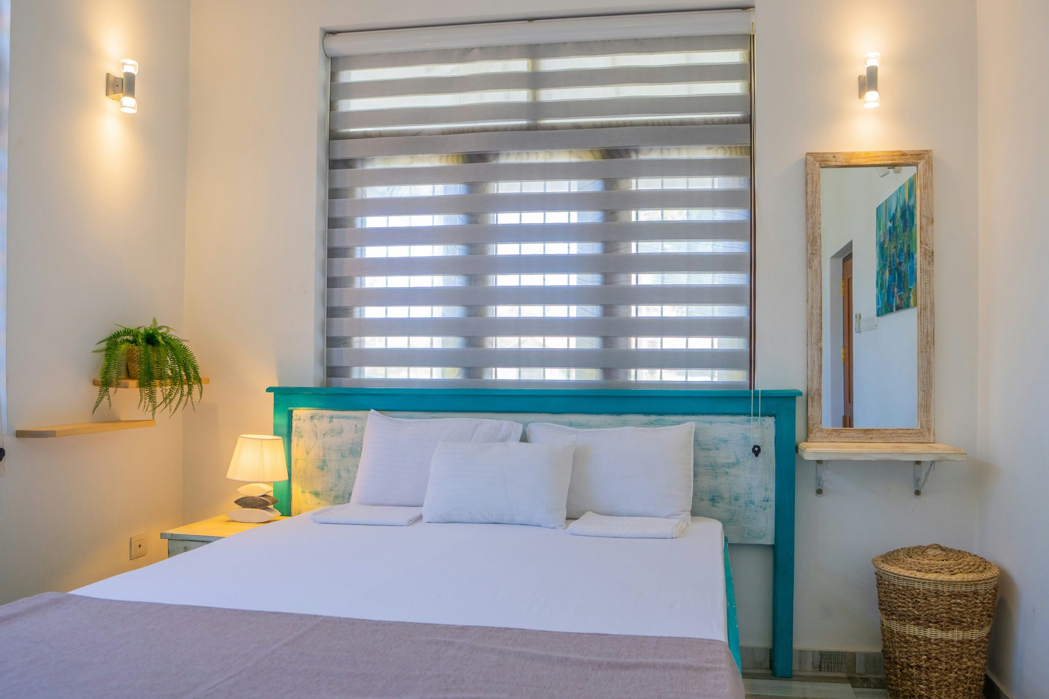 Bright and airy bedroom interior with a turquoise rustic headboard, white linens, soft lighting, and natural decor elements like a hanging plant and wicker basket. A serene, minimalist space with trop