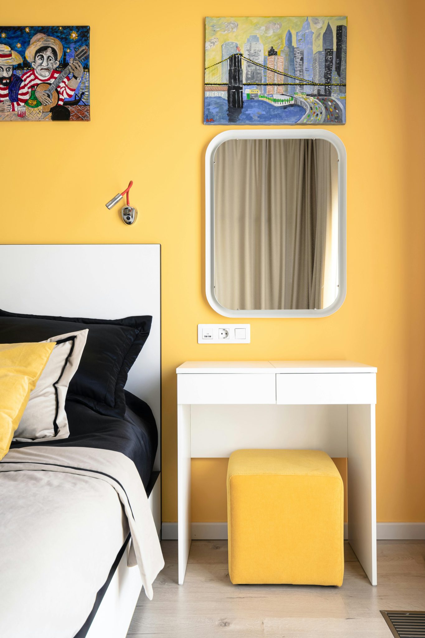 Bright and stylish bedroom featuring yellow walls, a small desk, mirror, and artwork.
