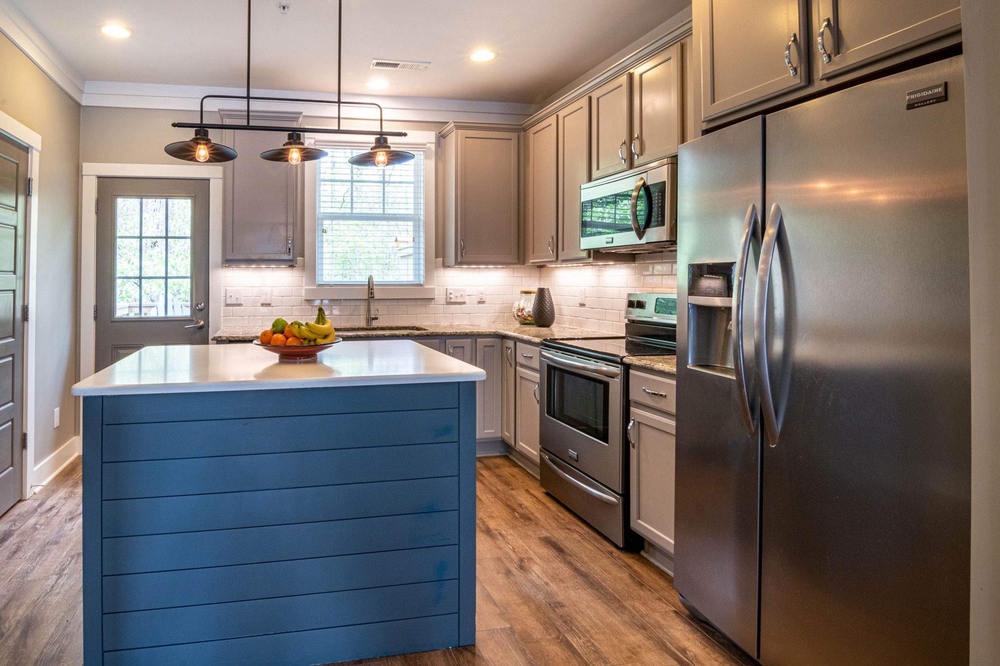 Bright and stylish kitchen featuring a blue island, stainless steel appliances, and modern lighting.