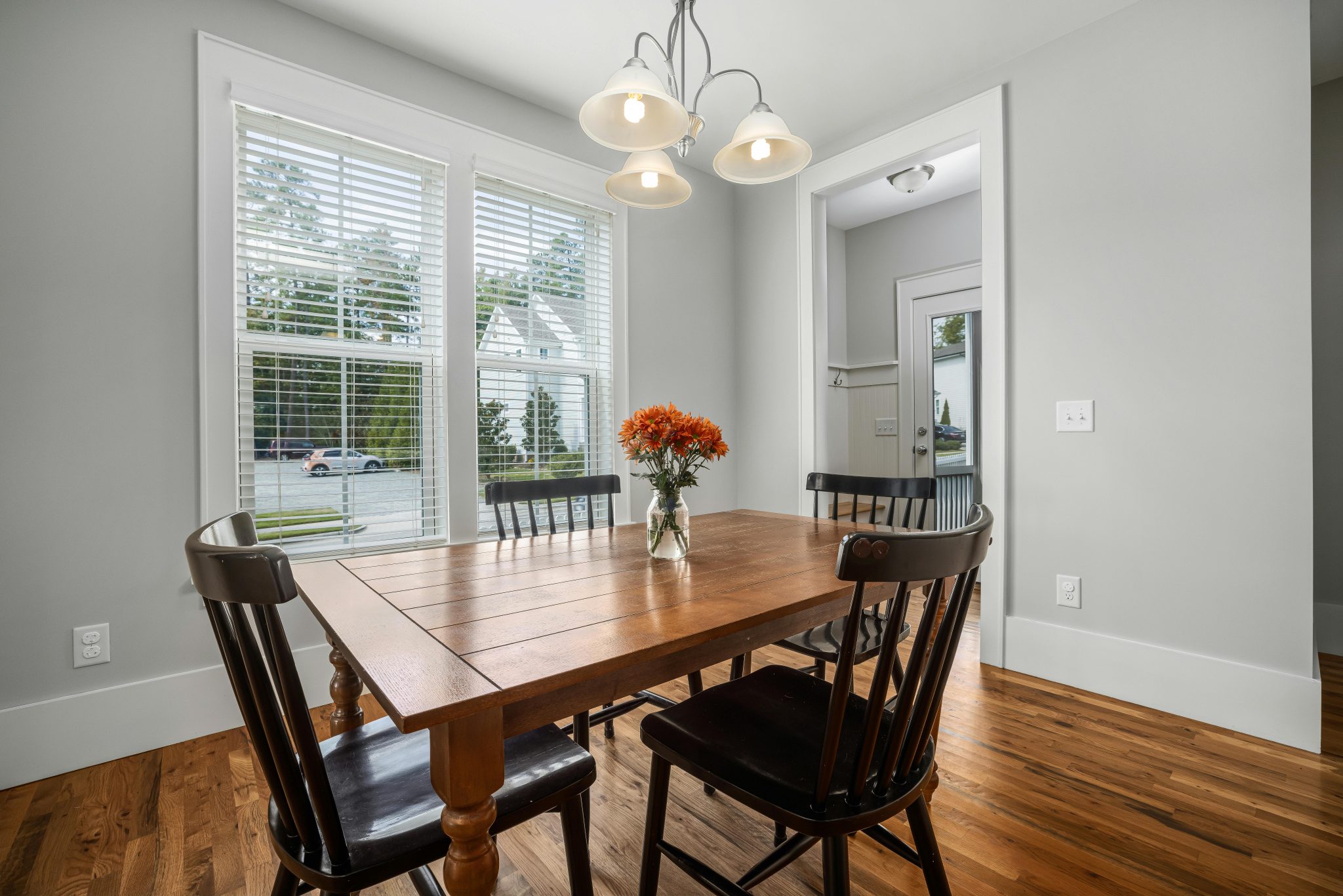 Bright dining room featuring a wooden table, chairs, flower vase, and modern ceiling lamp.