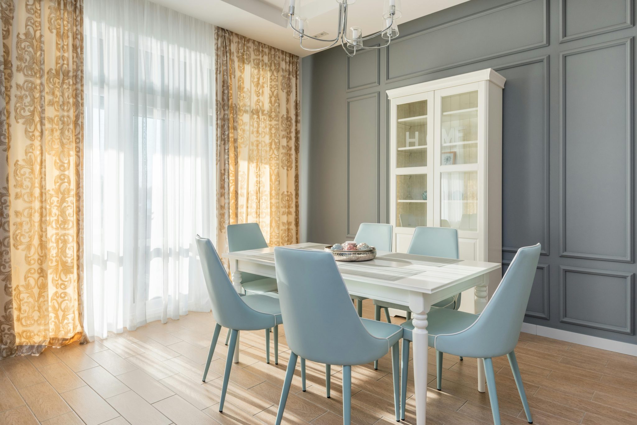 Bright dining room interior with blue chairs, white table, and decorative curtains.