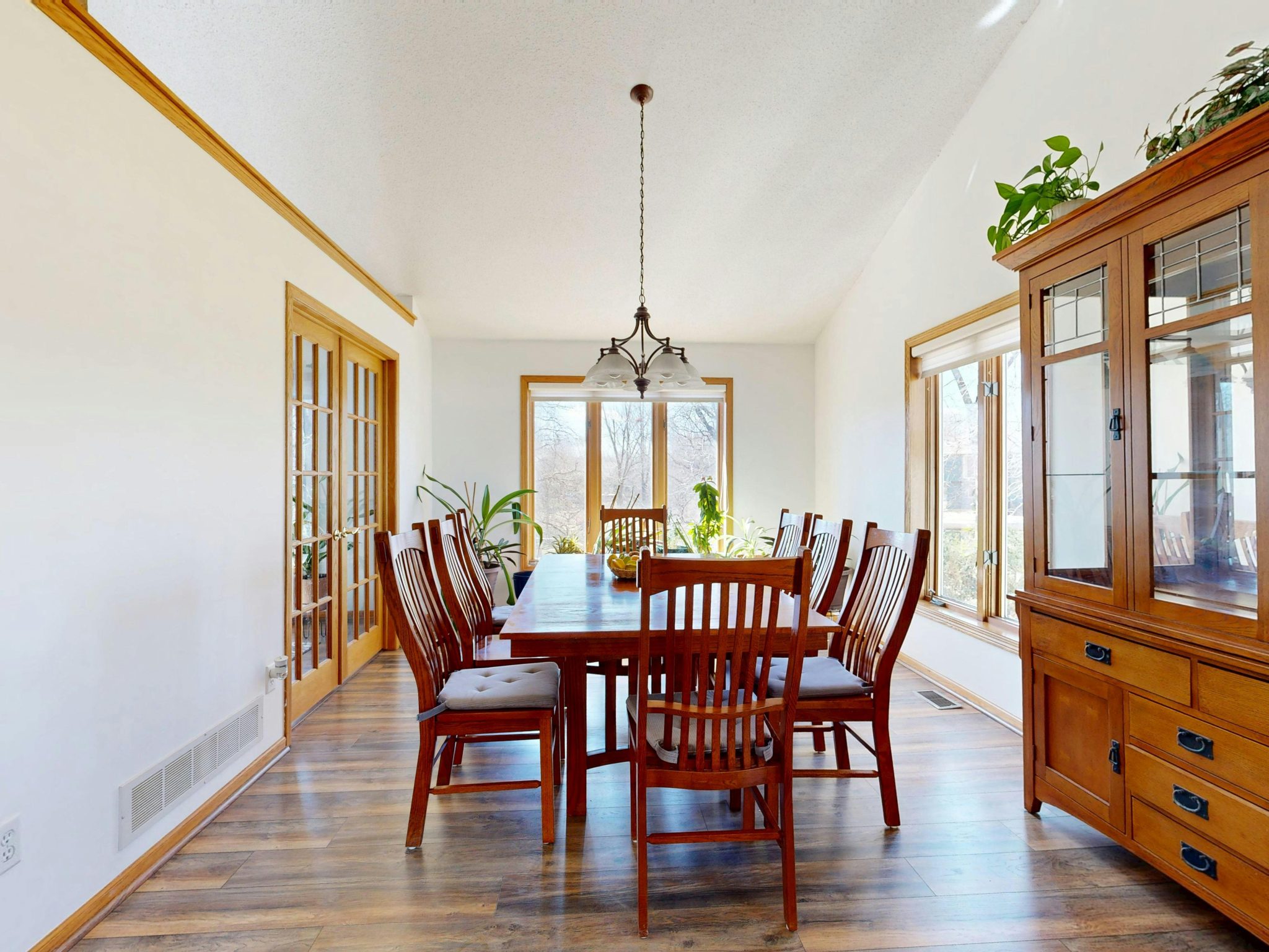 Bright dining room with wooden table, chairs, and cabinet under a hanging light fixture.