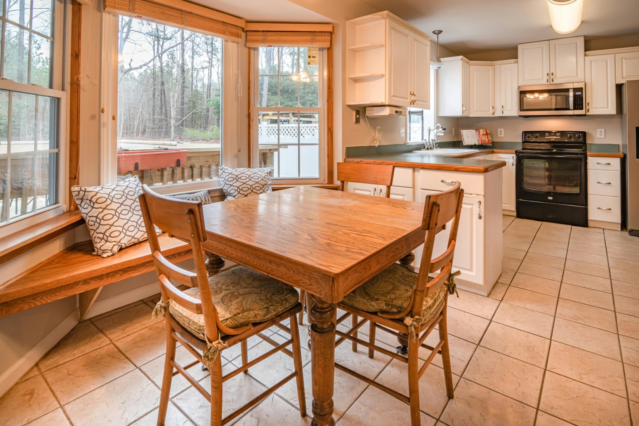 Bright kitchen with wooden dining table, chairs, and large windows offering natural light.
