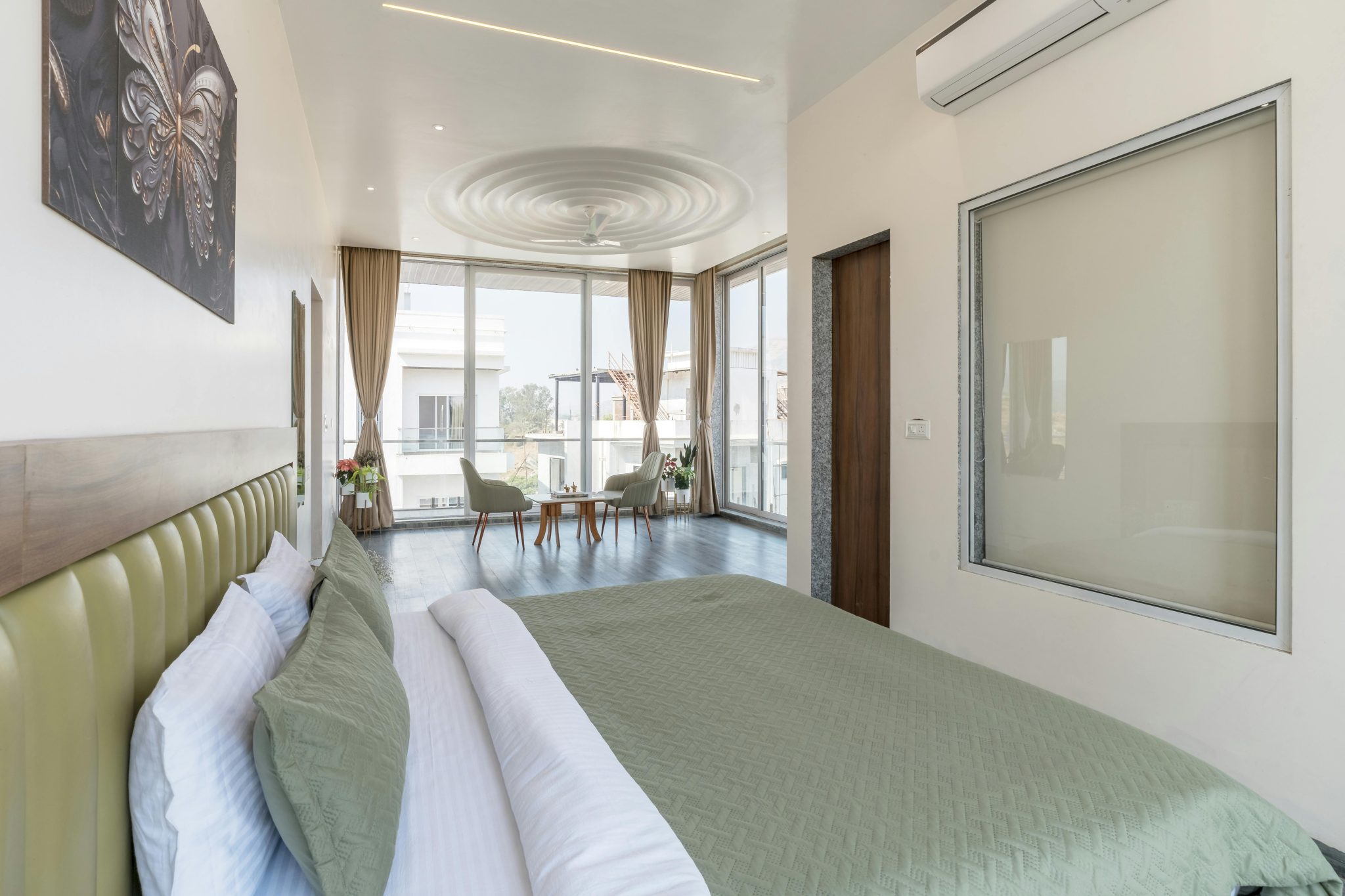 Bright modern bedroom with green bedding and large windows offering natural light.