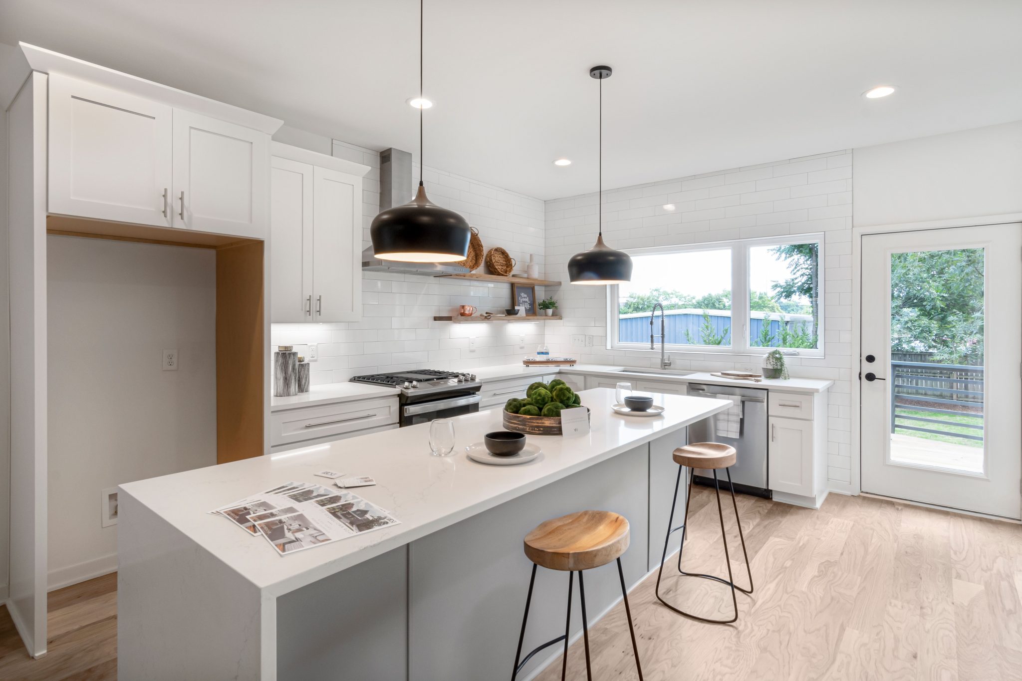 Bright modern kitchen with white cabinetry, wooden stools, and pendant lighting.