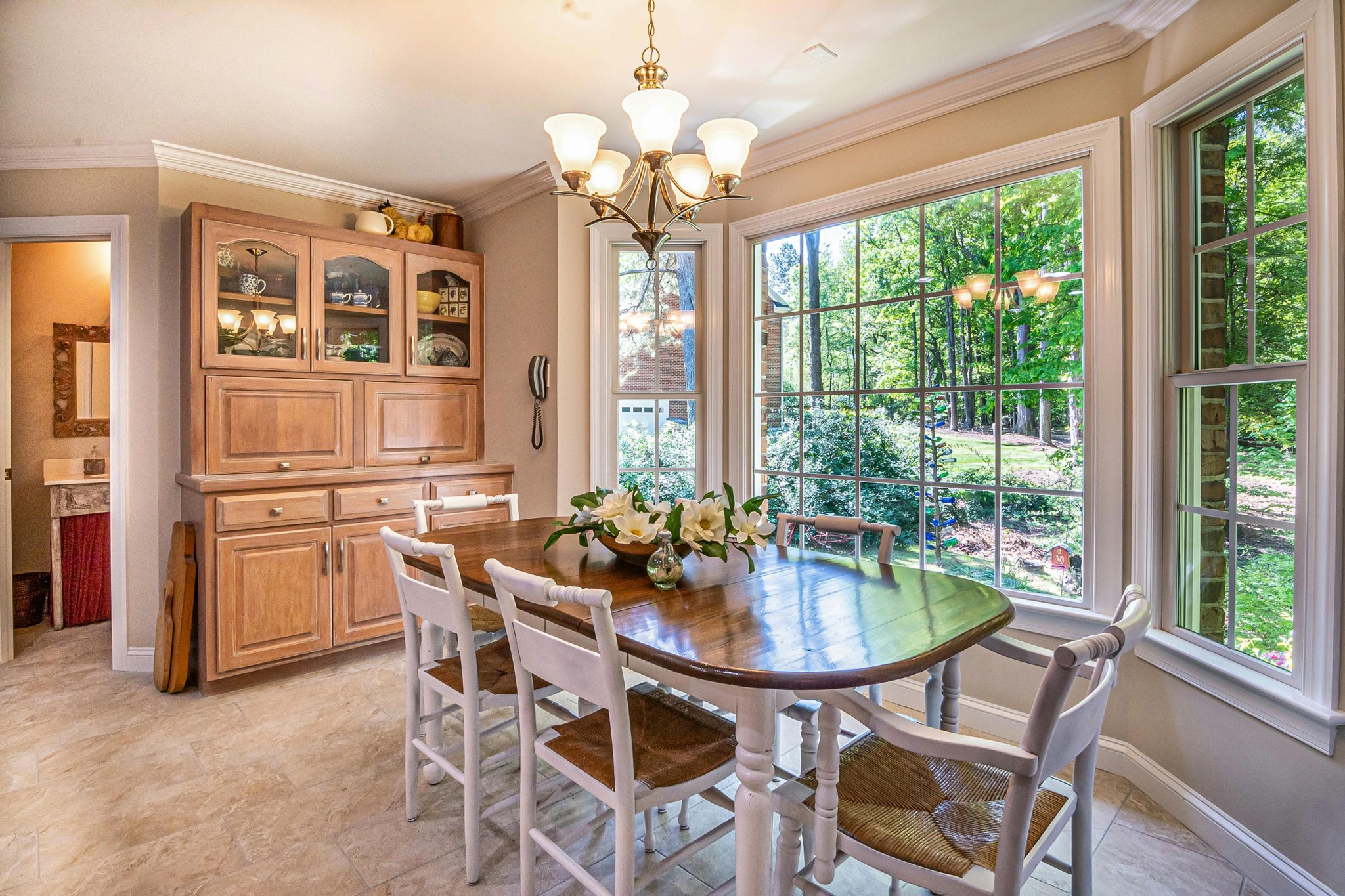 Charming dining area with wooden table and chairs overlooking a lush garden through large windows.