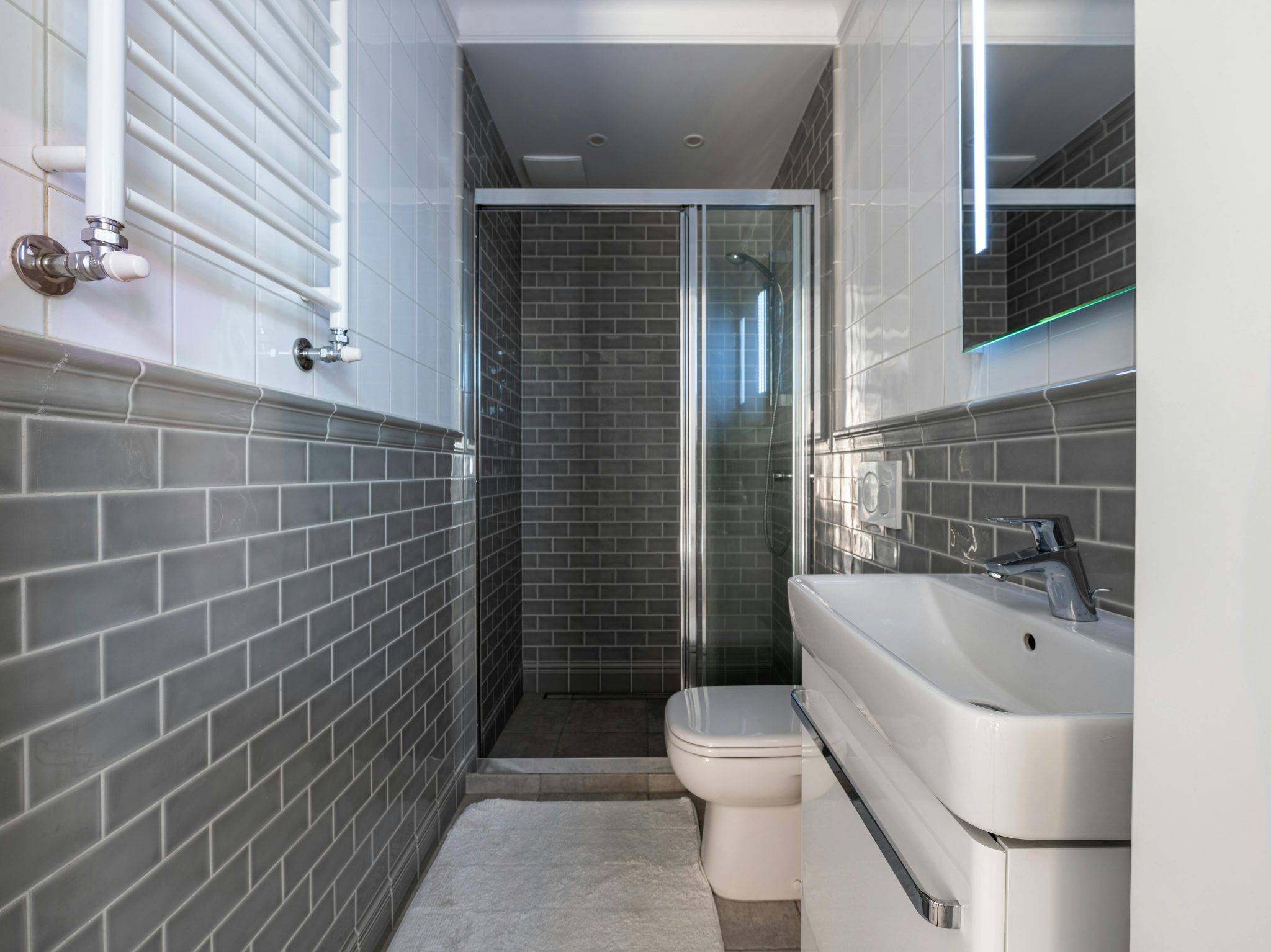 Compact bathroom featuring sleek fixtures and gray subway tiles with a glass-enclosed shower area.