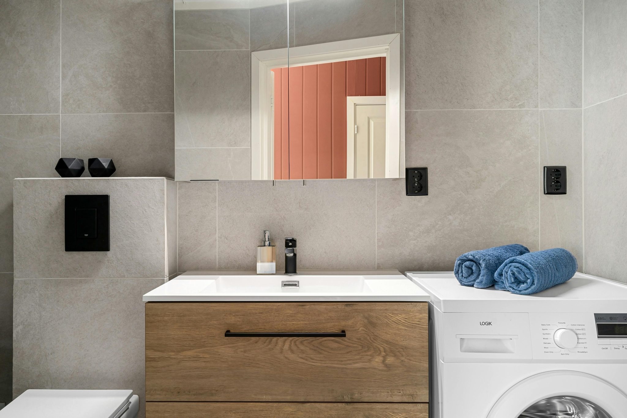 Contemporary bathroom featuring a sleek wooden vanity, washing machine, and modern fixtures.
