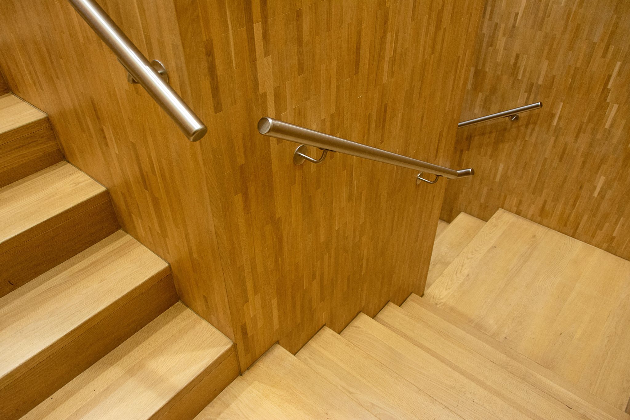 Contemporary wooden staircase with sleek metal handrails in an indoor setting.