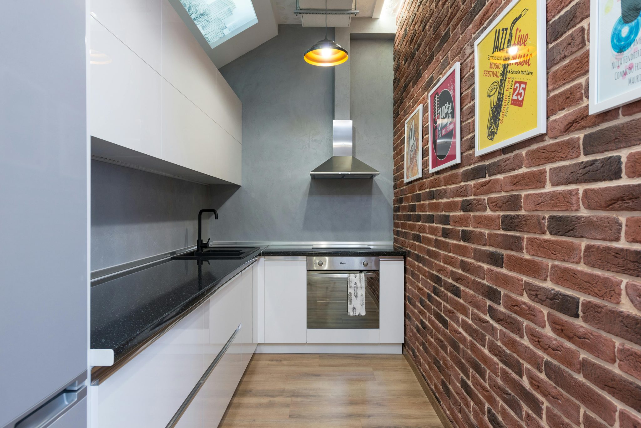 Counter with sink and white cupboards near metal extractor hood and oven in small stylish kitchen with pictures in modern apartment