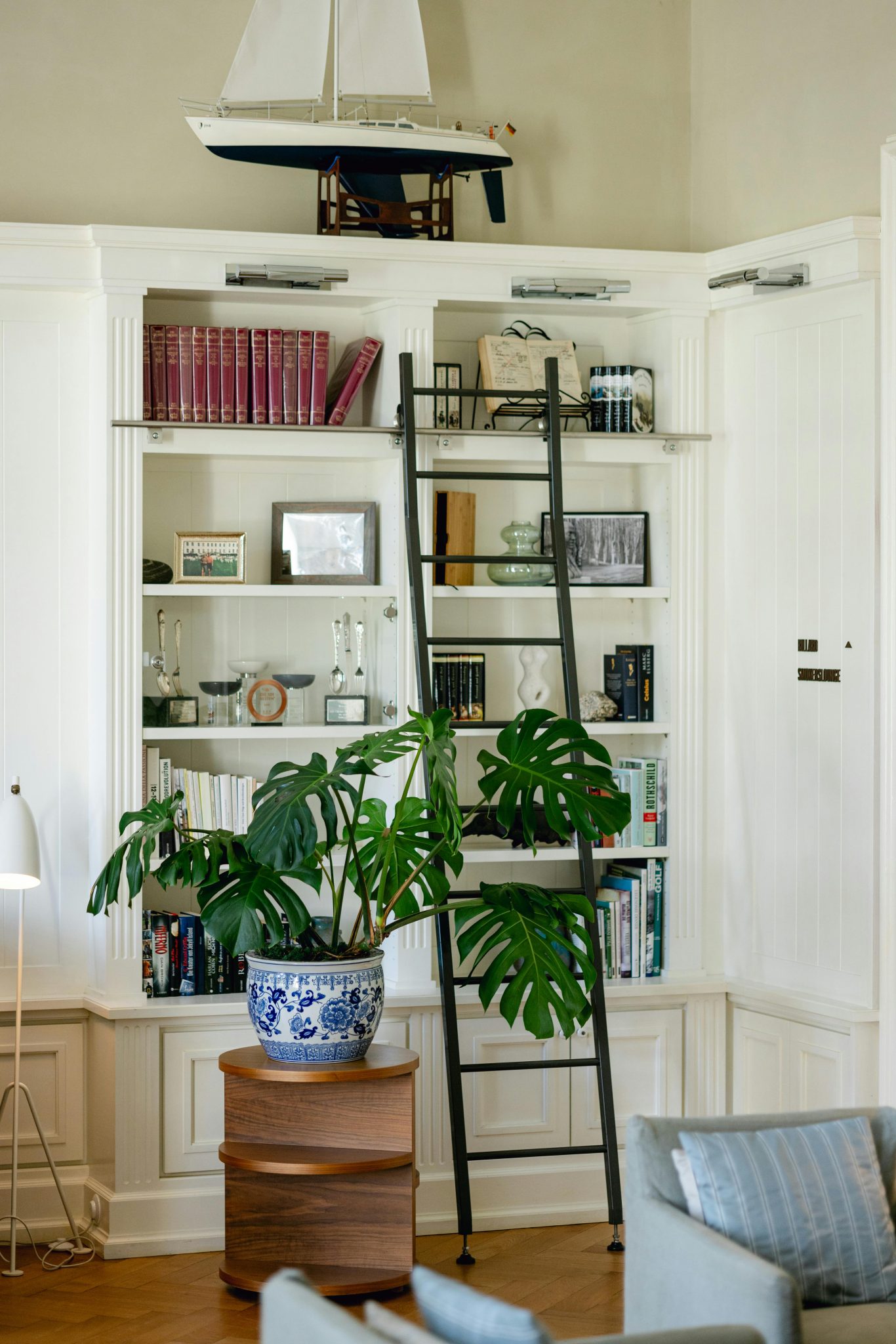 Cozy and chic living room featuring a white bookshelf, ladder, and a Monstera plant, exuding sophistication.
