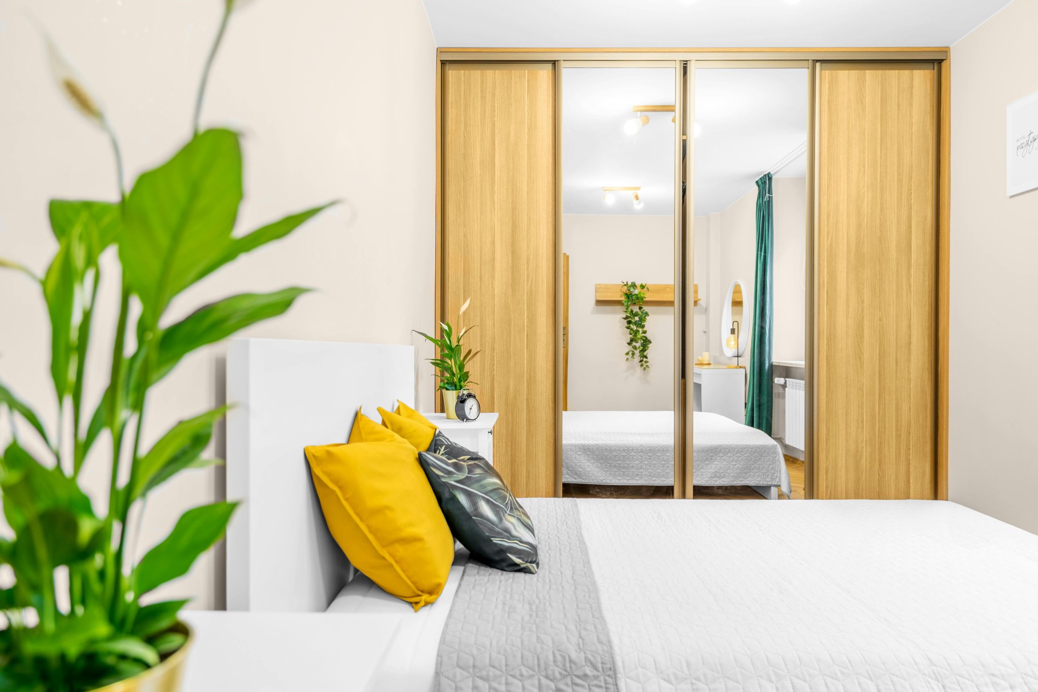 Cozy bedroom interior with modern decor, mirror closet, and vibrant plant accents.