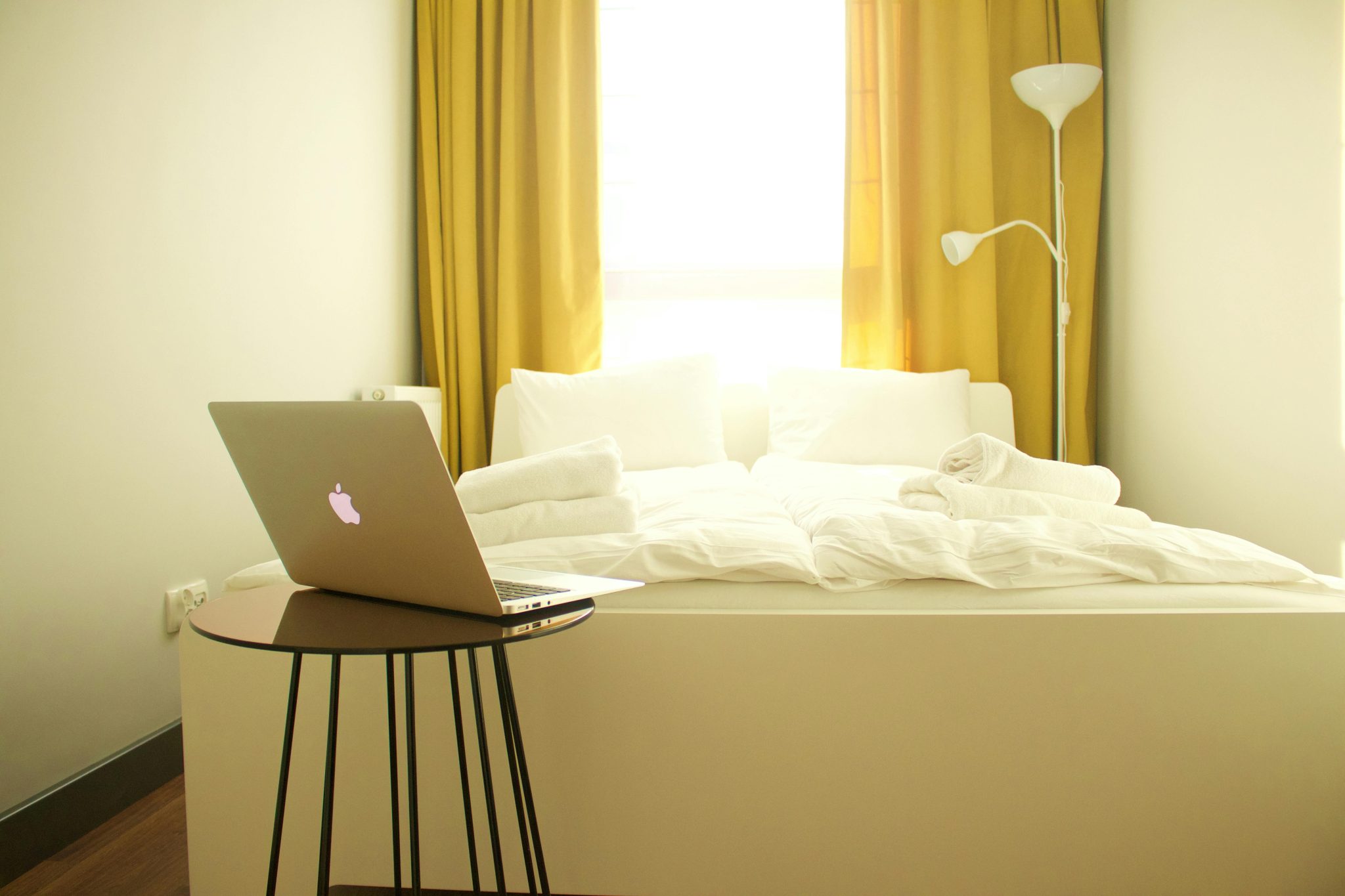 Cozy bedroom with a laptop, yellow curtains, and contemporary decor.