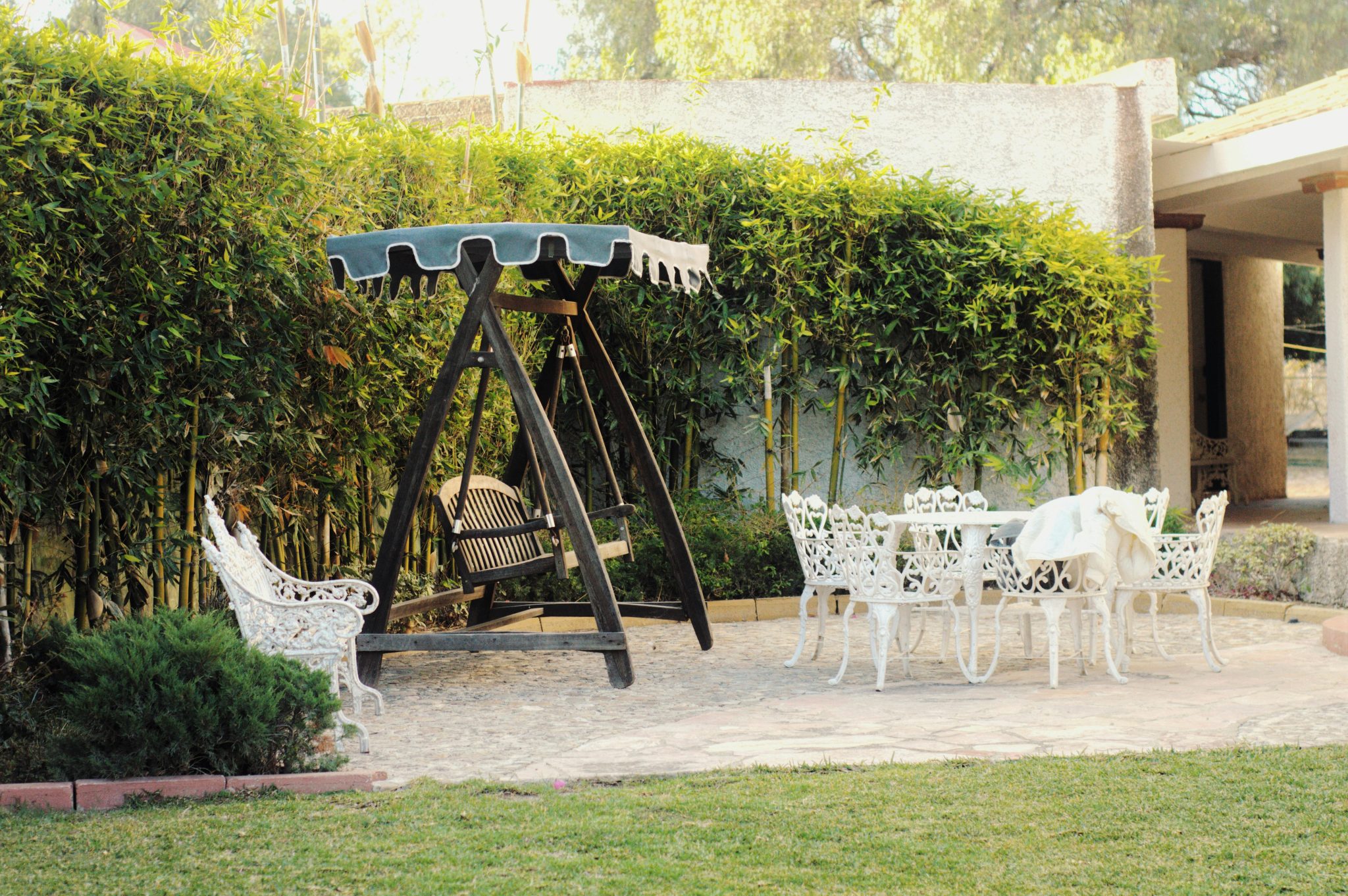 Cozy outdoor patio with vintage furniture and swing, surrounded by lush greenery.