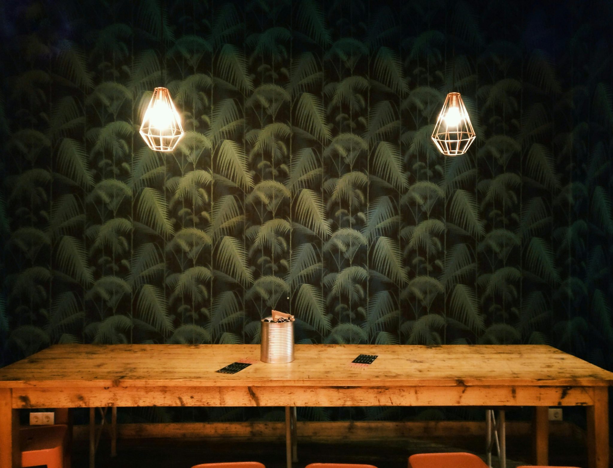 Cozy rustic interior featuring geometric pendant lamps and a large wooden table against a patterned wall.
