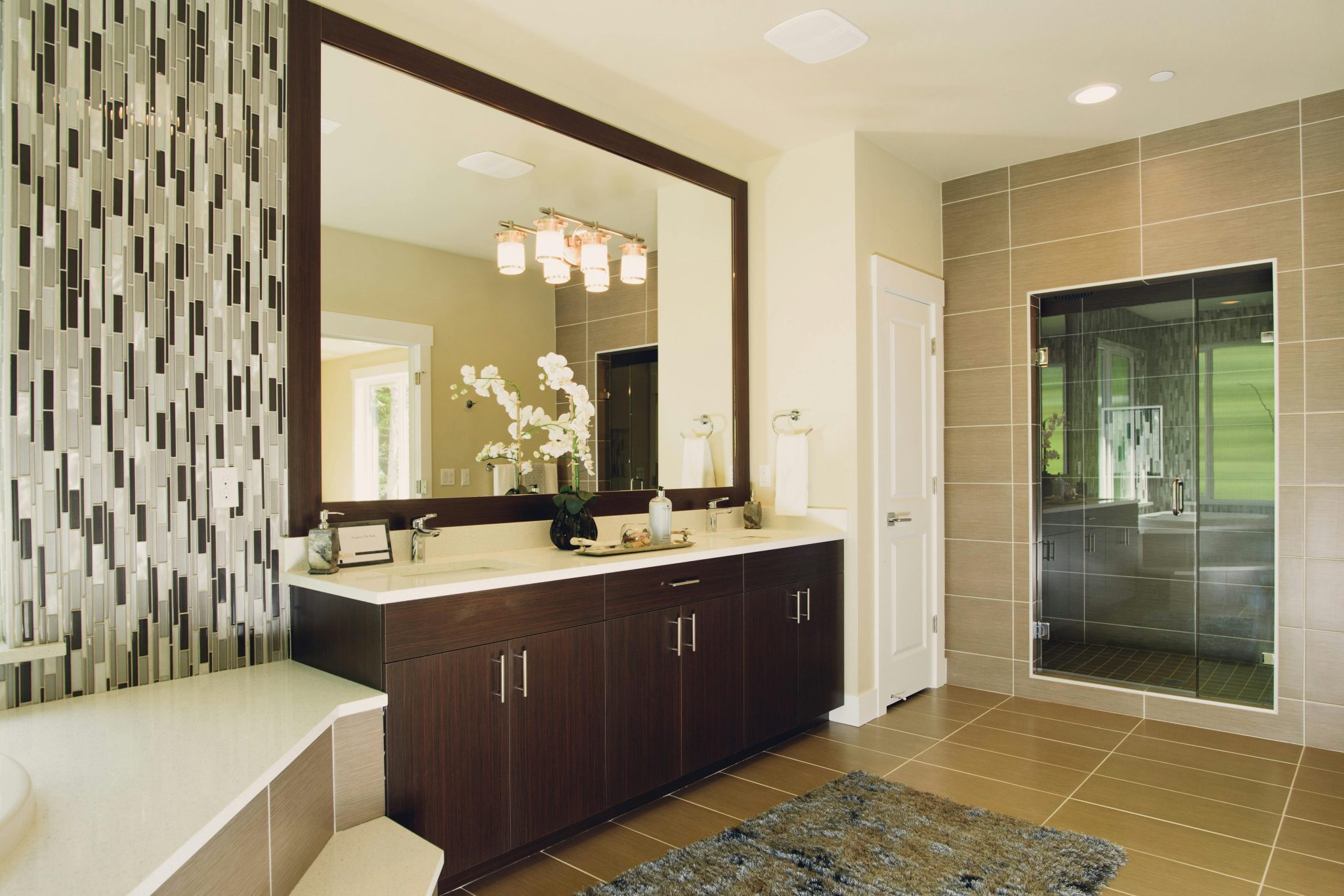 Elegant bathroom featuring modern sink and shower with decorative tiling and large mirror.