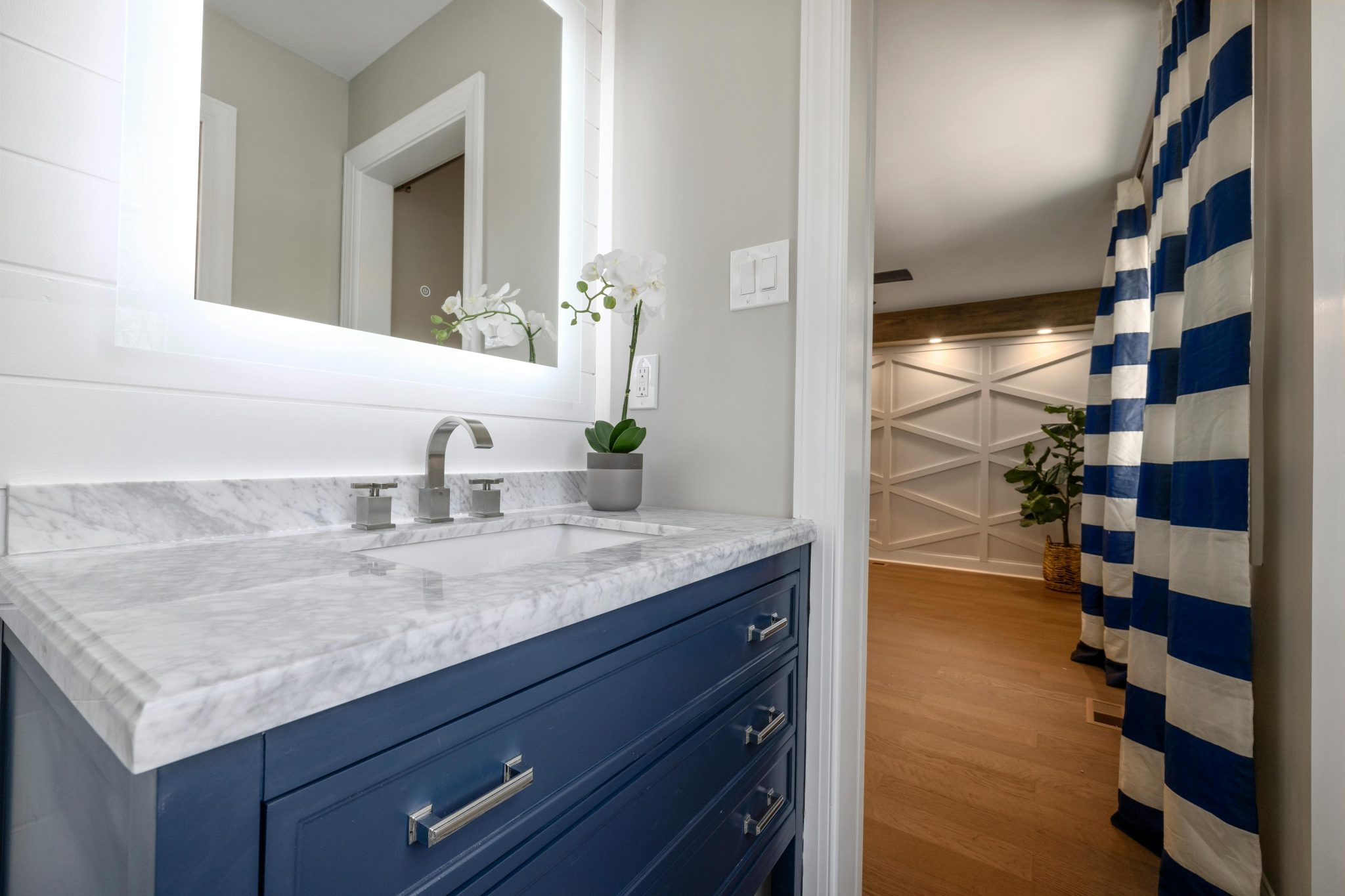 Elegant bathroom interior with marble vanity, illuminated mirror, and blue accents for a contemporary feel.