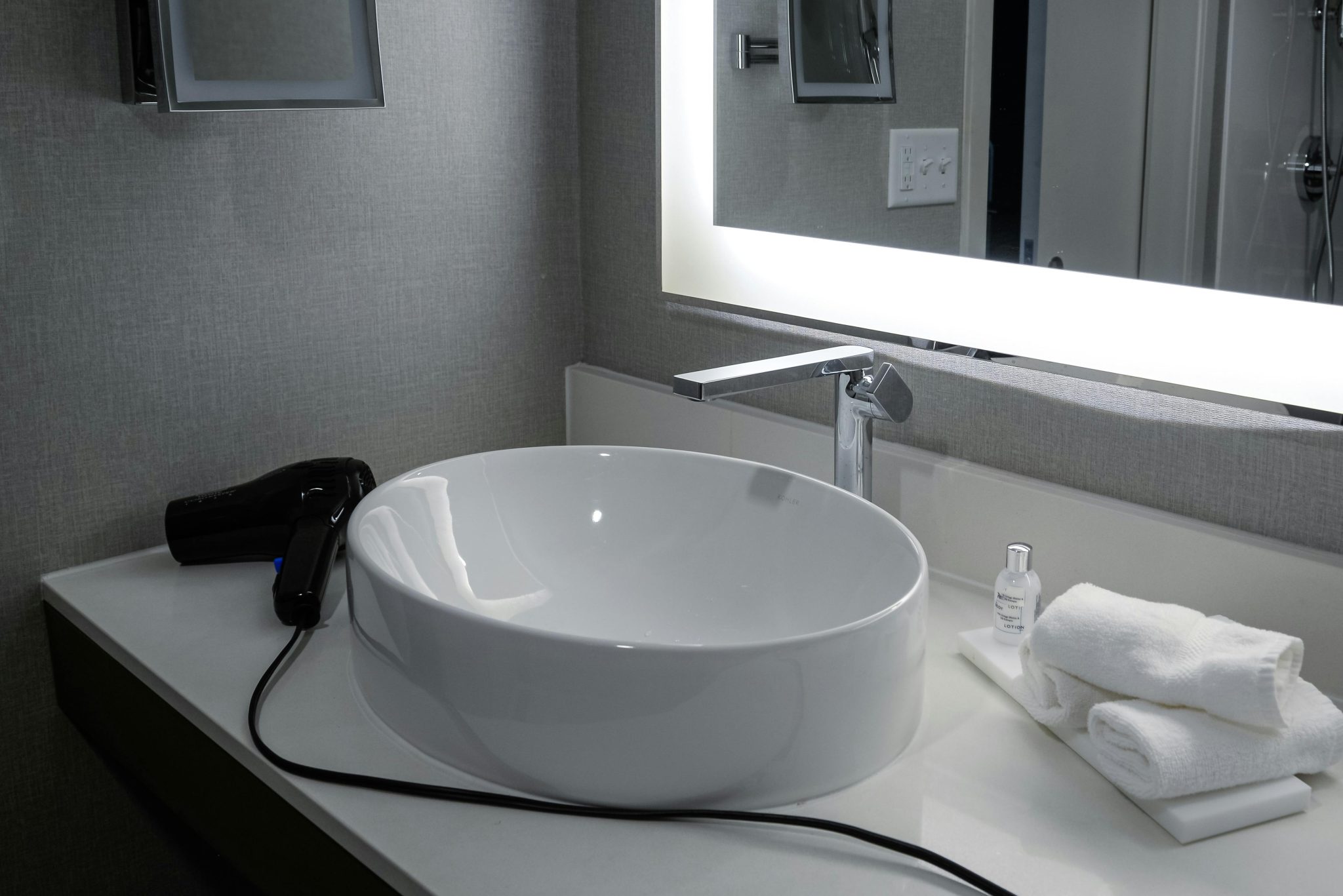 Elegant bathroom vanity with bowl sink, lighted mirror, and hairdryer in a hotel setting.