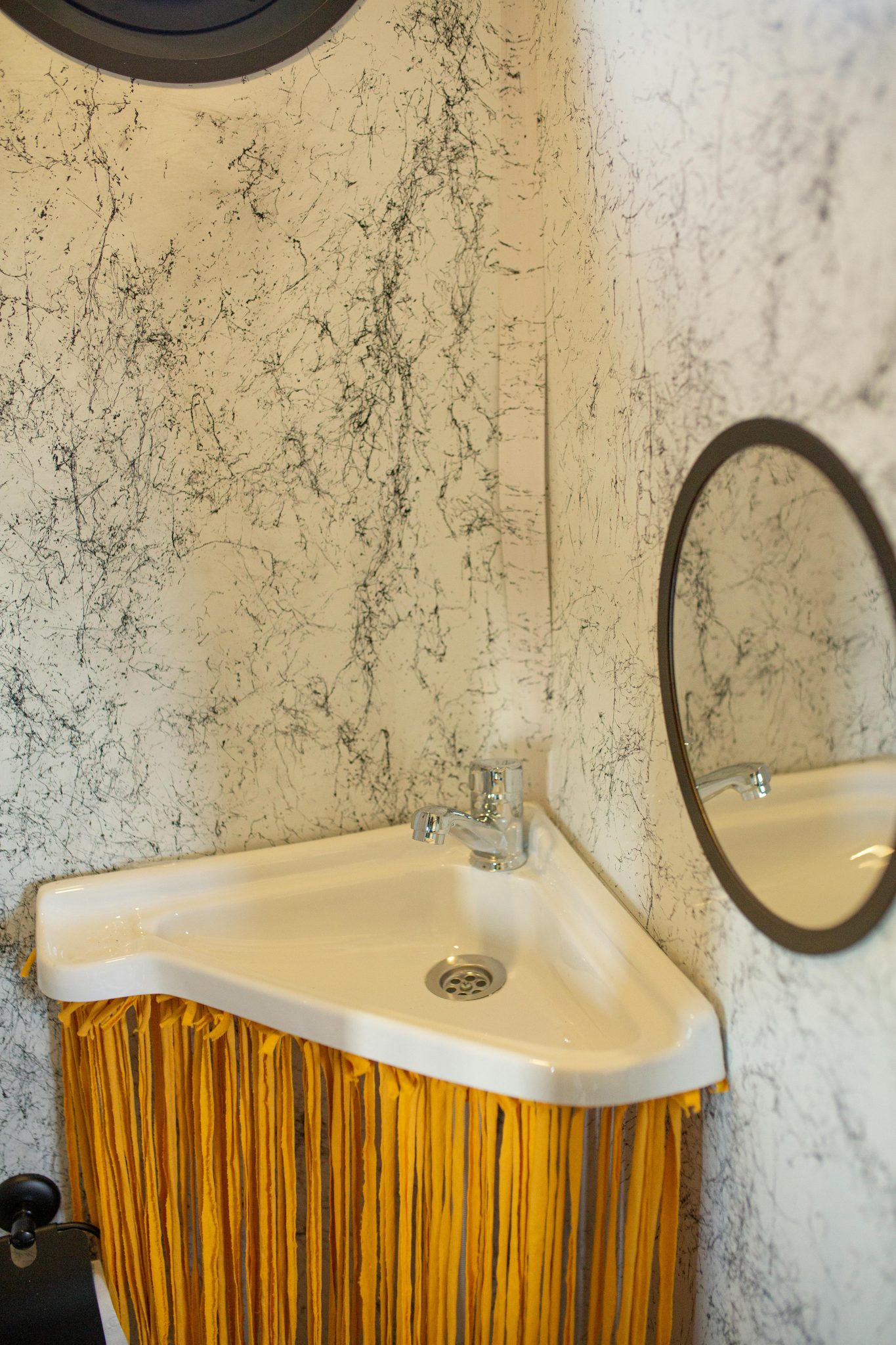 Elegant corner bathroom sink with a round mirror and marble textured walls.