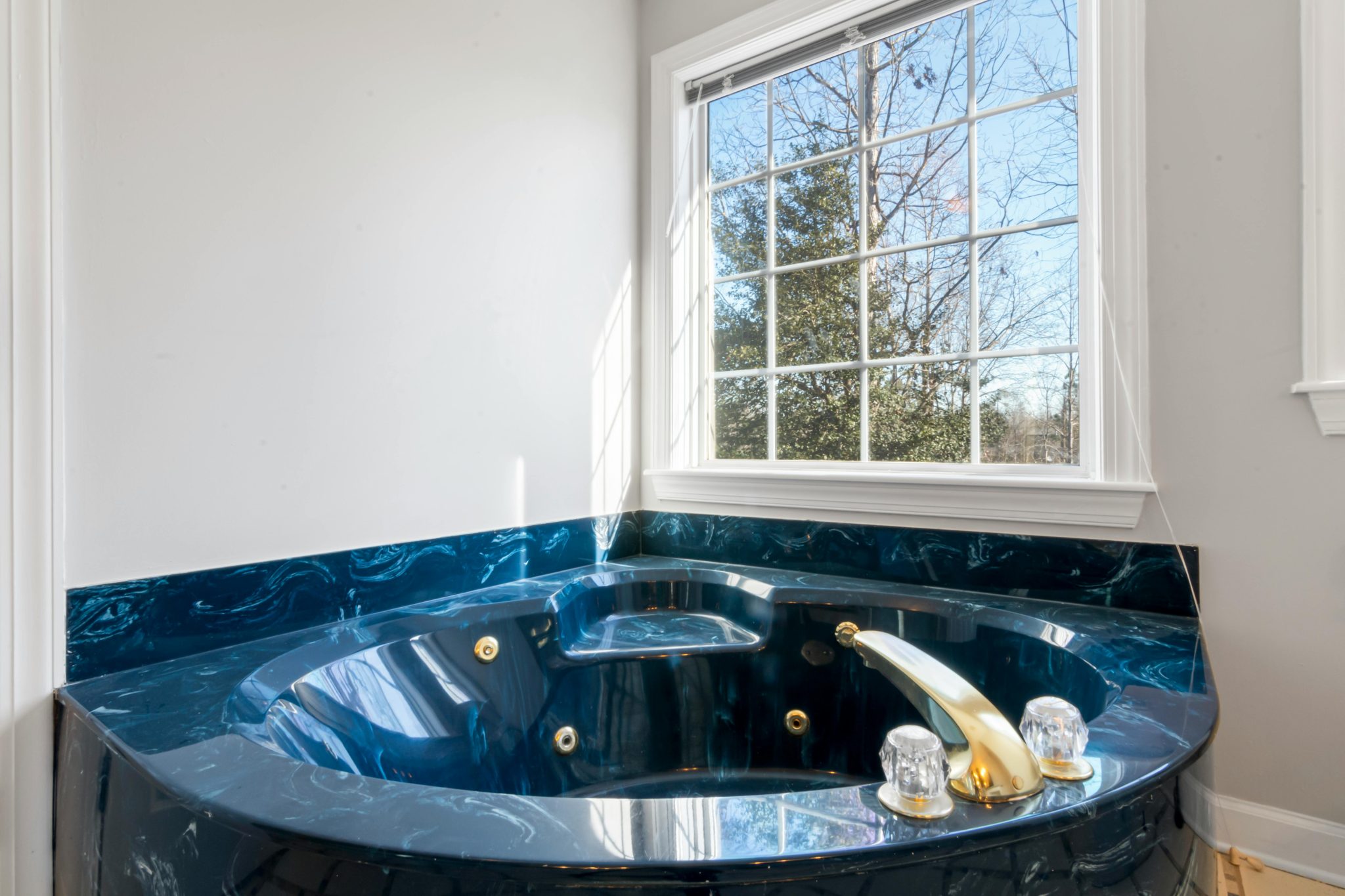 Elegant corner bathtub with blue marble and gold fixtures, near a window with a scenic view.
