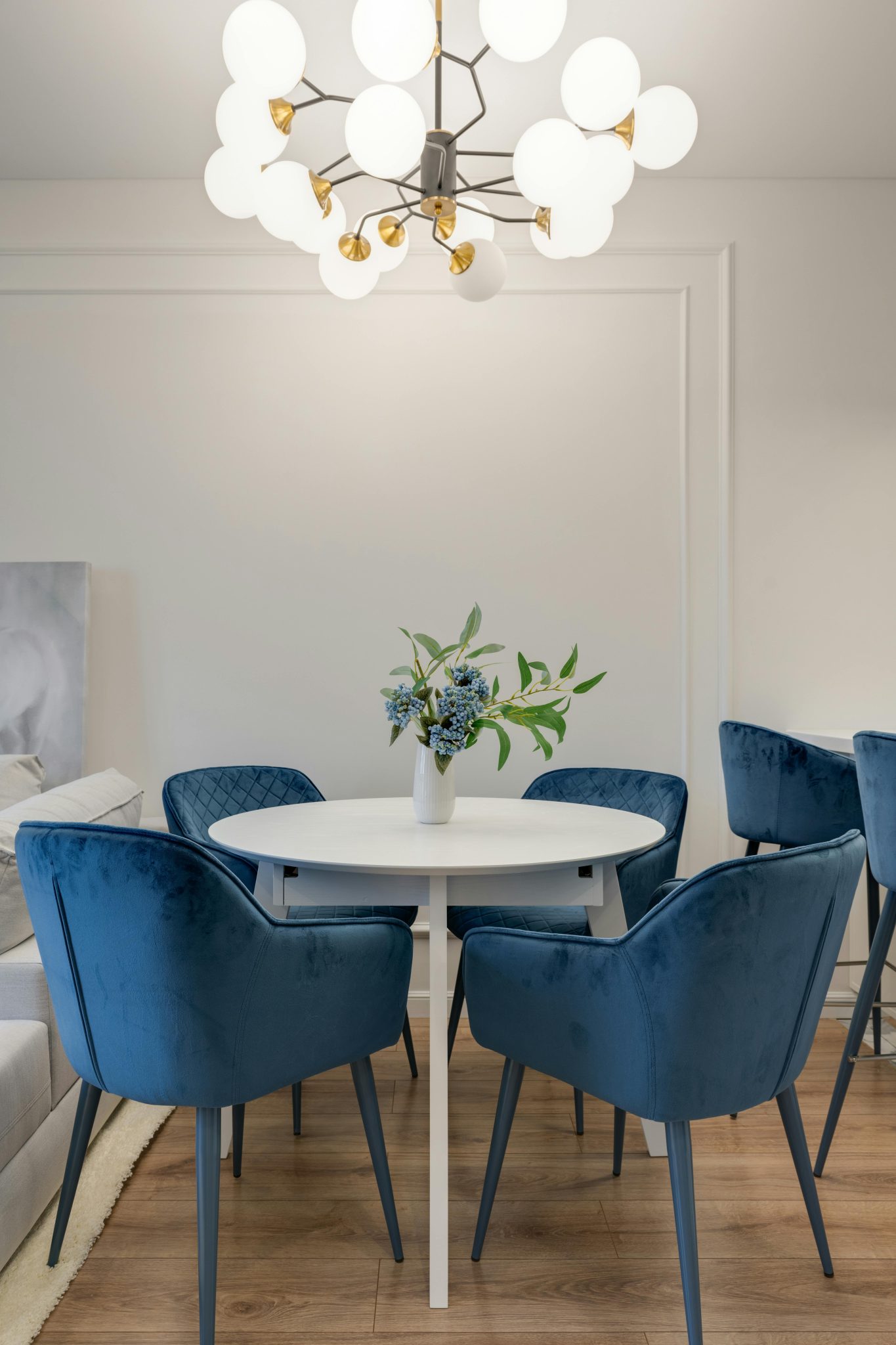 Elegant dining area featuring blue velvet chairs, round table, and stylish chandelier lighting.
