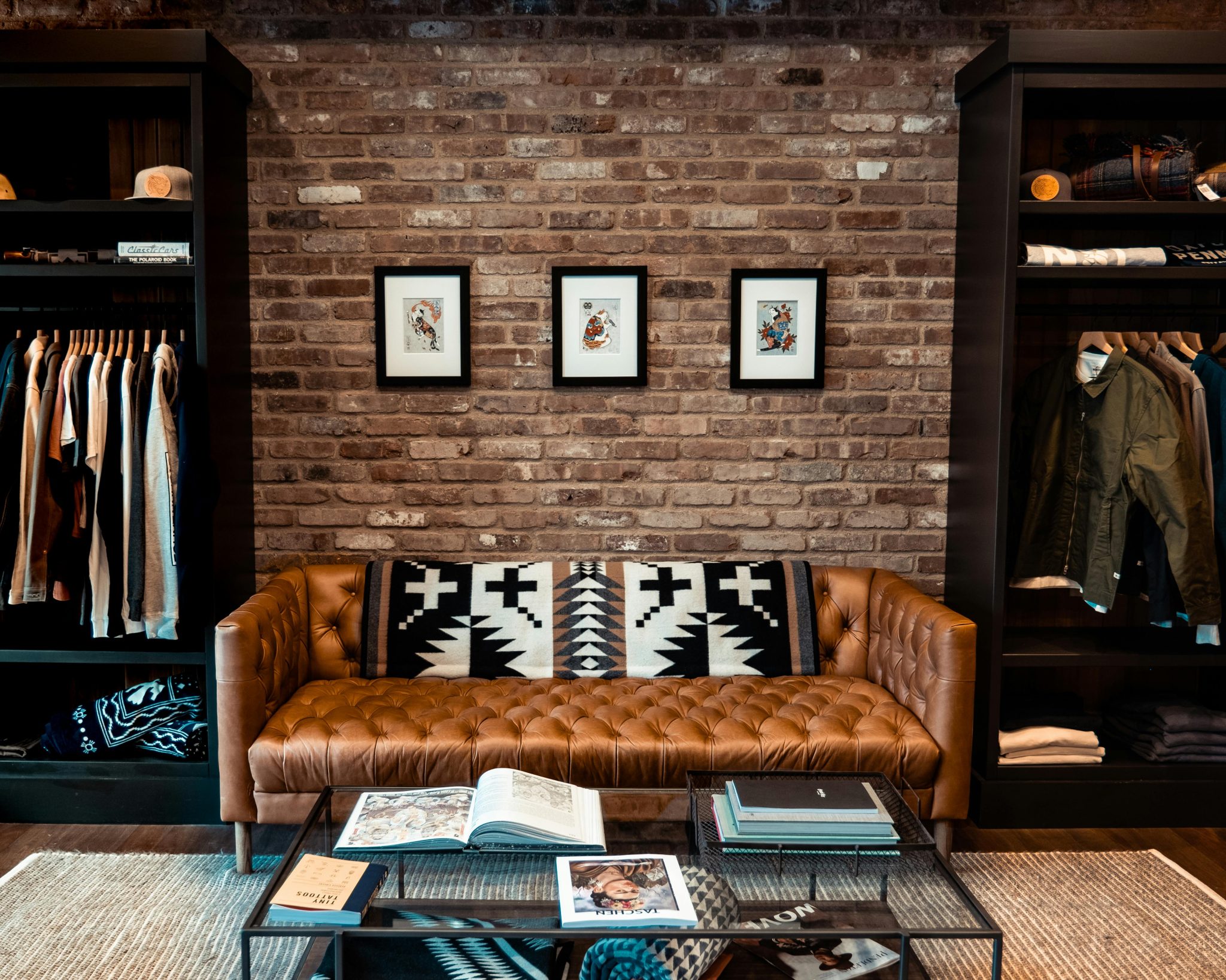 Elegant living room with brown leather couch, brick wall, art, and modern decor.