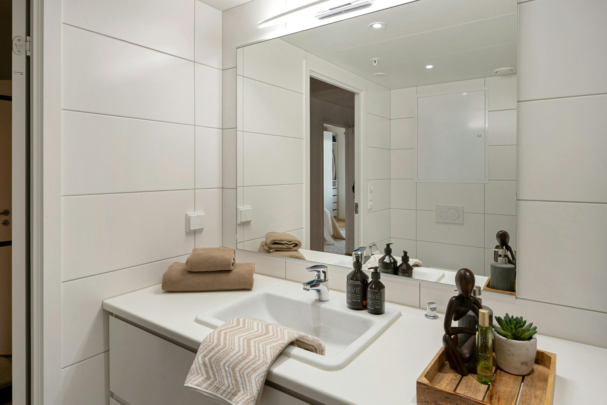 Elegant modern bathroom with white tiles, large mirror, and stylish accessories like towels and toiletries enhancing the decor.
