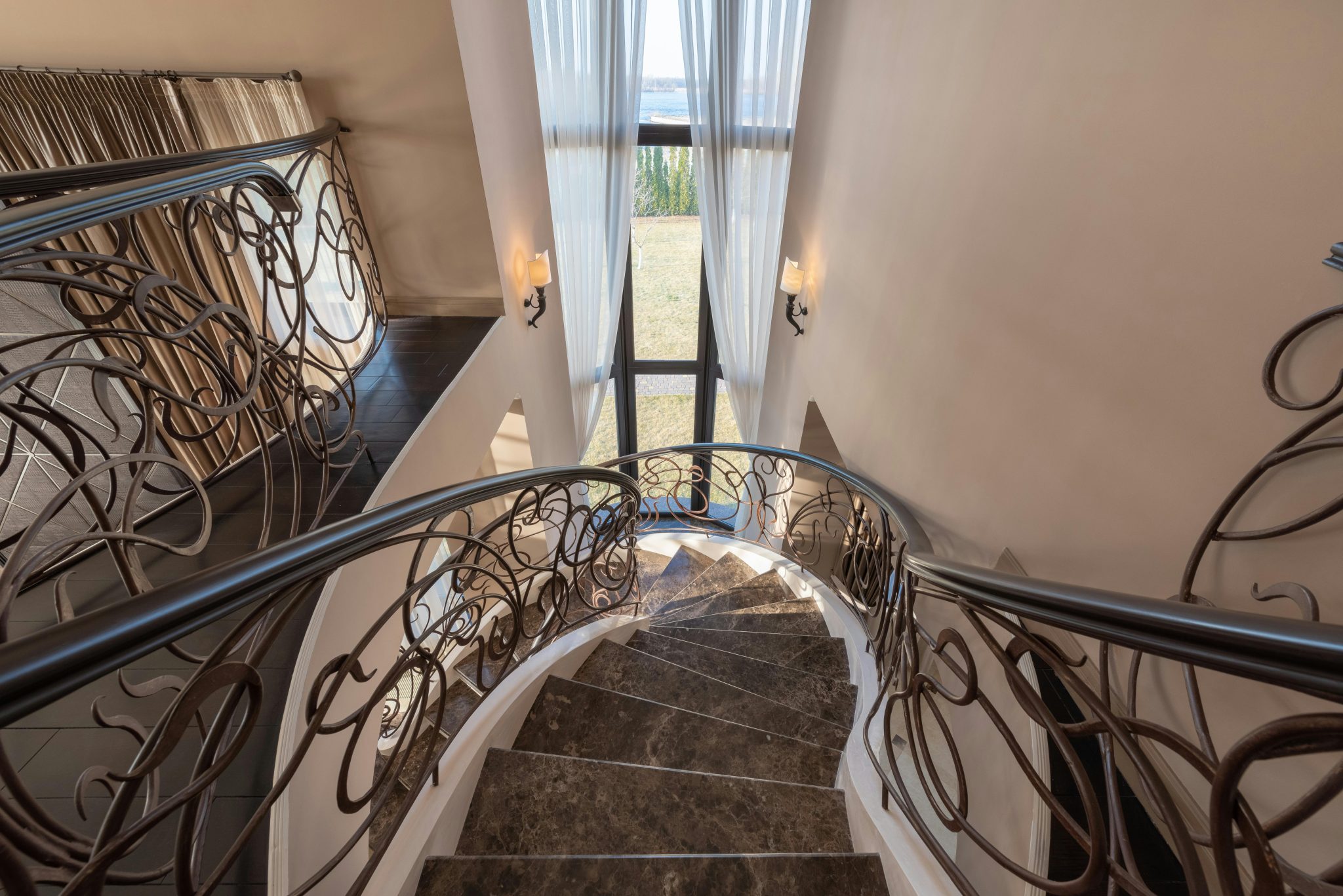 From above of stairway with marble steps and metal railings with ornamental elements located near window with tulle in contemporary building