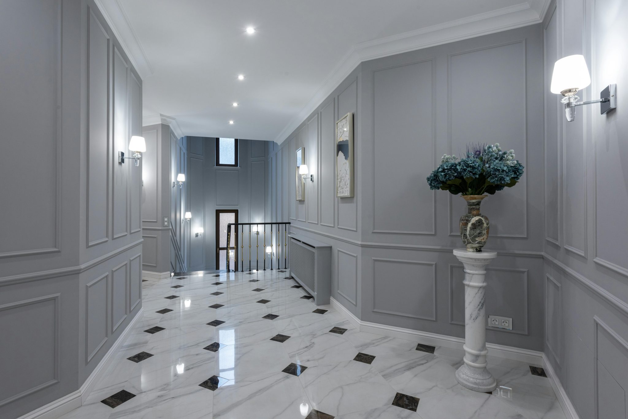 Gray walls and shiny marble floor in hallway of spacious classic styled villa decorated with paintings and lamps